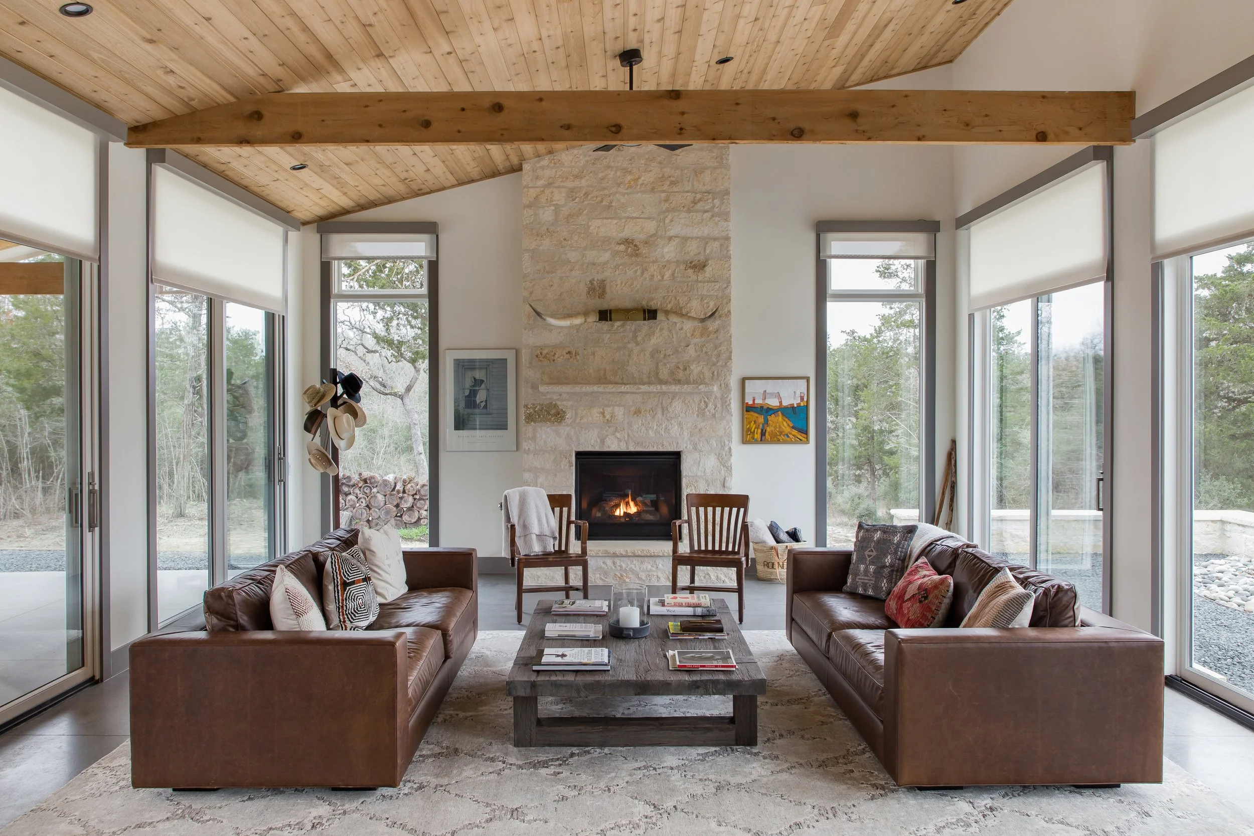 Living room with large windows, two leather sofas, a fireplace, and wooden ceiling and beams.