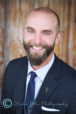 Well groomed beard and neat haircut, dark suit with subtle pinstripe, nice complementing shirt and tie (blue brings out his blue eyes), Background is outdoors adds a bit of casual feel to the photo.