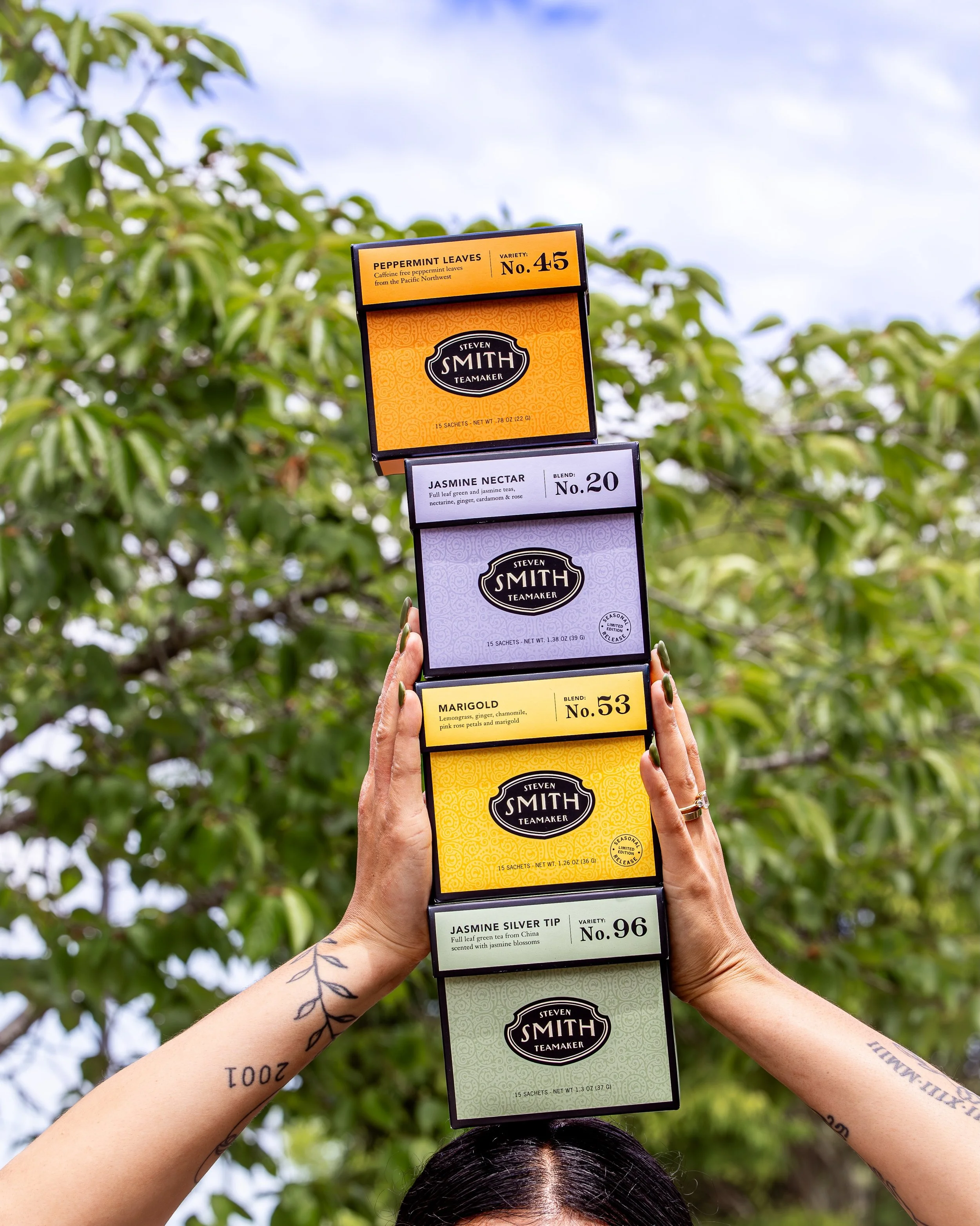 Tip top tea boxes on the tip top of a head! 🫖 An unconvential way to drink tea, but an excellent way to show off our gorgeous retail selections of tea from @smithteamaker! 🧡💜💛💚. From herbal, calming options like Peppermint and Marigold, to refre