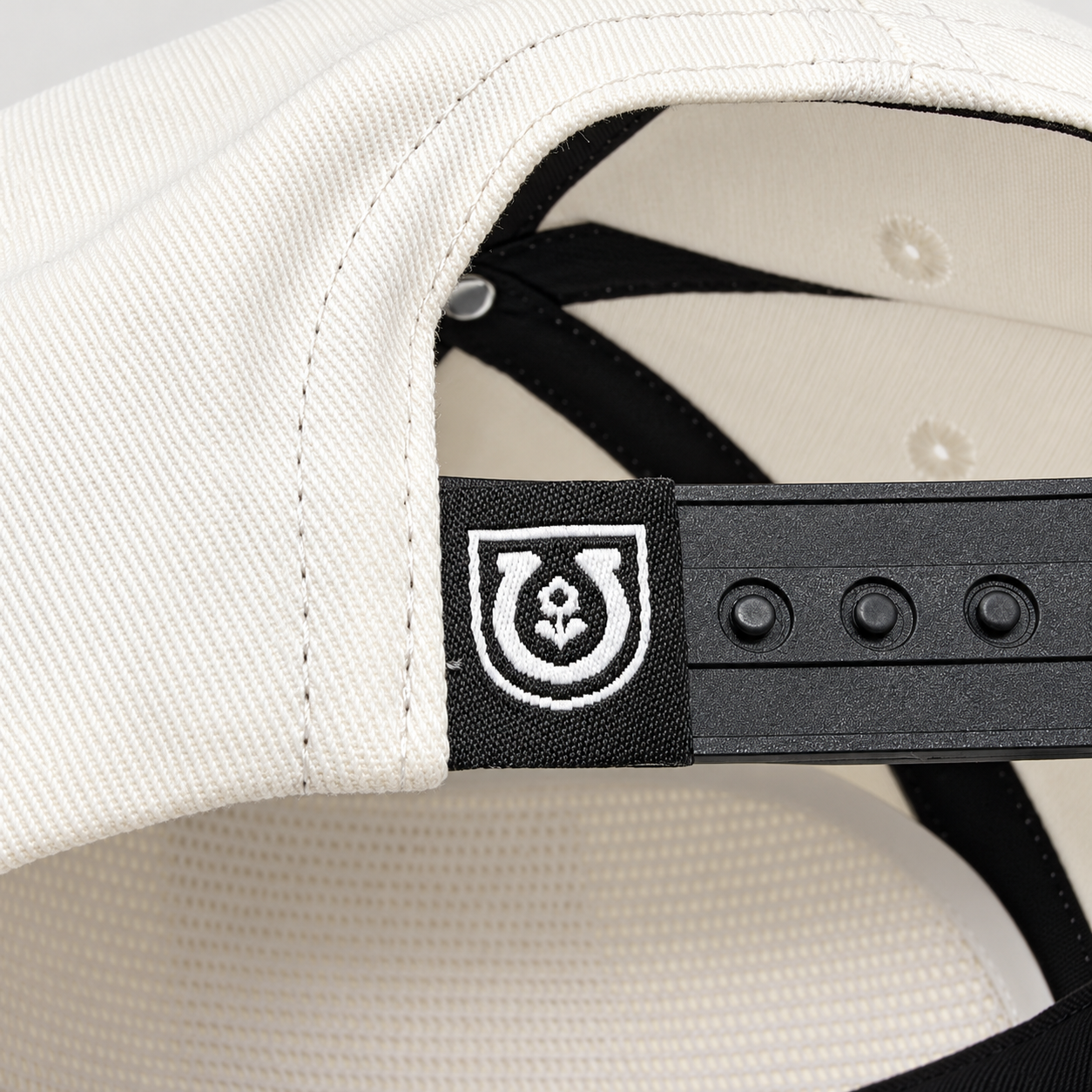 Adjustable black snapback closure and woven horseshoe label on the off-white Mike Tabie Work Horse cotton cap.