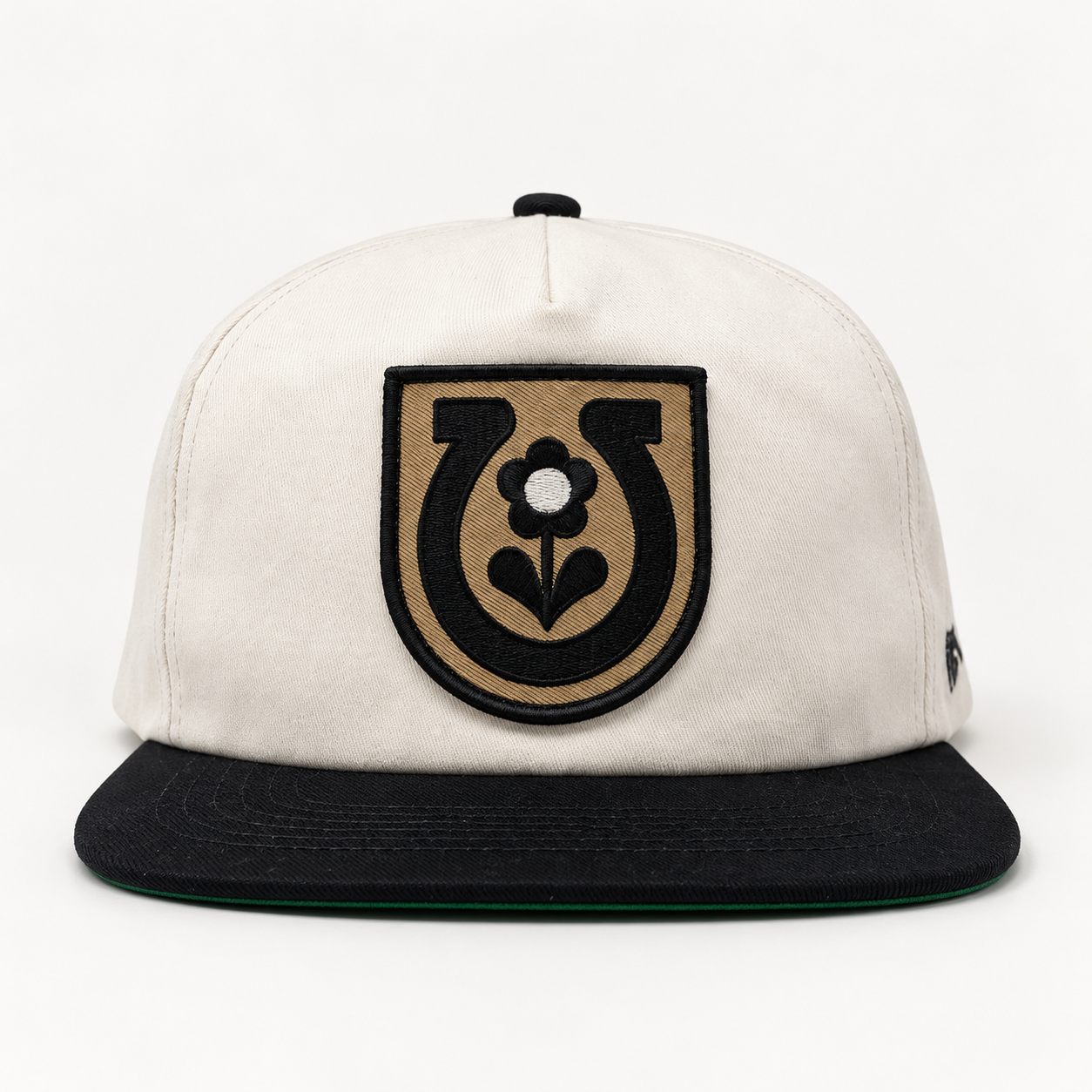 Front view of the Grizzly Wheeler × Mike Tabie Work Horse cotton cap with off-white crown, black brim, and horseshoe-and-flower patch.
