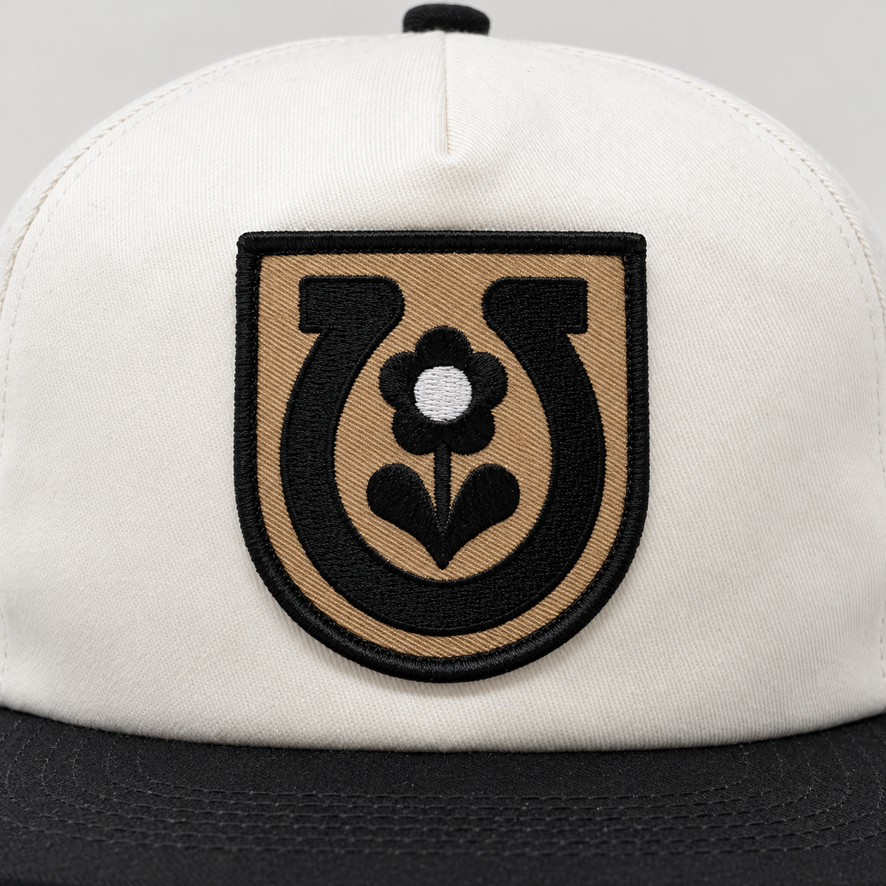 Close-up of the embroidered black horseshoe and flower on the tan front patch of the Mike Tabie Work Horse cap.