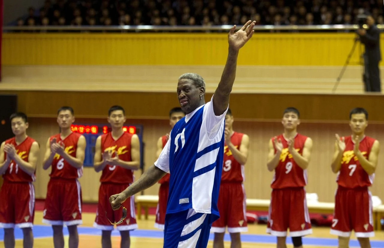 Dennis Rodman waves at North Korean leader Kim Jong Un, seated above in the stands, after singing 'Happy Birthday' to him before an exhibition basketball game at an indoor stadium in Pyongyang, North Korea, in January 2014. (AP/Kim Kwang Hyon)