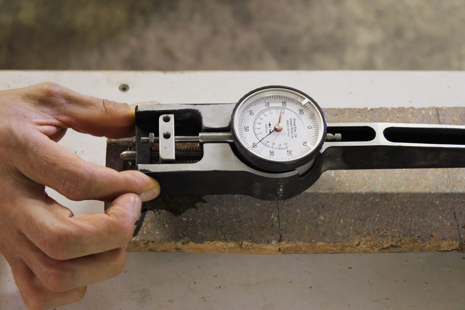 Measuring linear drying shrinkage a test sample of Watershed Materials’ geopolymer masonry using a strain gauge precise to the thousandth of a millimeter. The extremely precise measurements made by the strain gauge will be corrected based on temperature then compared against measurements of a tempered steel reference instrument. Clays, by nature, tend to shrink and swell upon drying and wetting, which can lead to problems when they are employed as construction materials. Mix design optimization and the modification of clay minerals through geopolymerization assists in overcoming many of the difficulties typically associated with clays and allows Watershed Materials to achieve minimal drying shrinkage in masonry products.