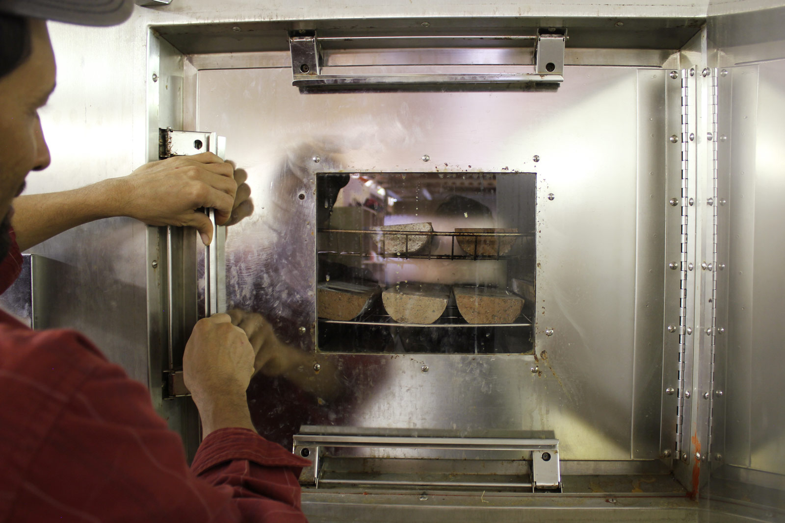 A technician checking test specimens in an environmental chamber. Curing conditions are fundamental to the success of Watershed Materials’ geopolymer masonry production. In the factory or on-site production facility, masonry curing will take place on racks adjacent to the production facility. Another benefit of Watershed Materials geopolymer technology are relatively low curing temperature requirements; waste heat from hydraulic motors used by the production machinery can be reclaimed to marginally raise ambient temperatures for curing, supplemented by solar heating where necessary.