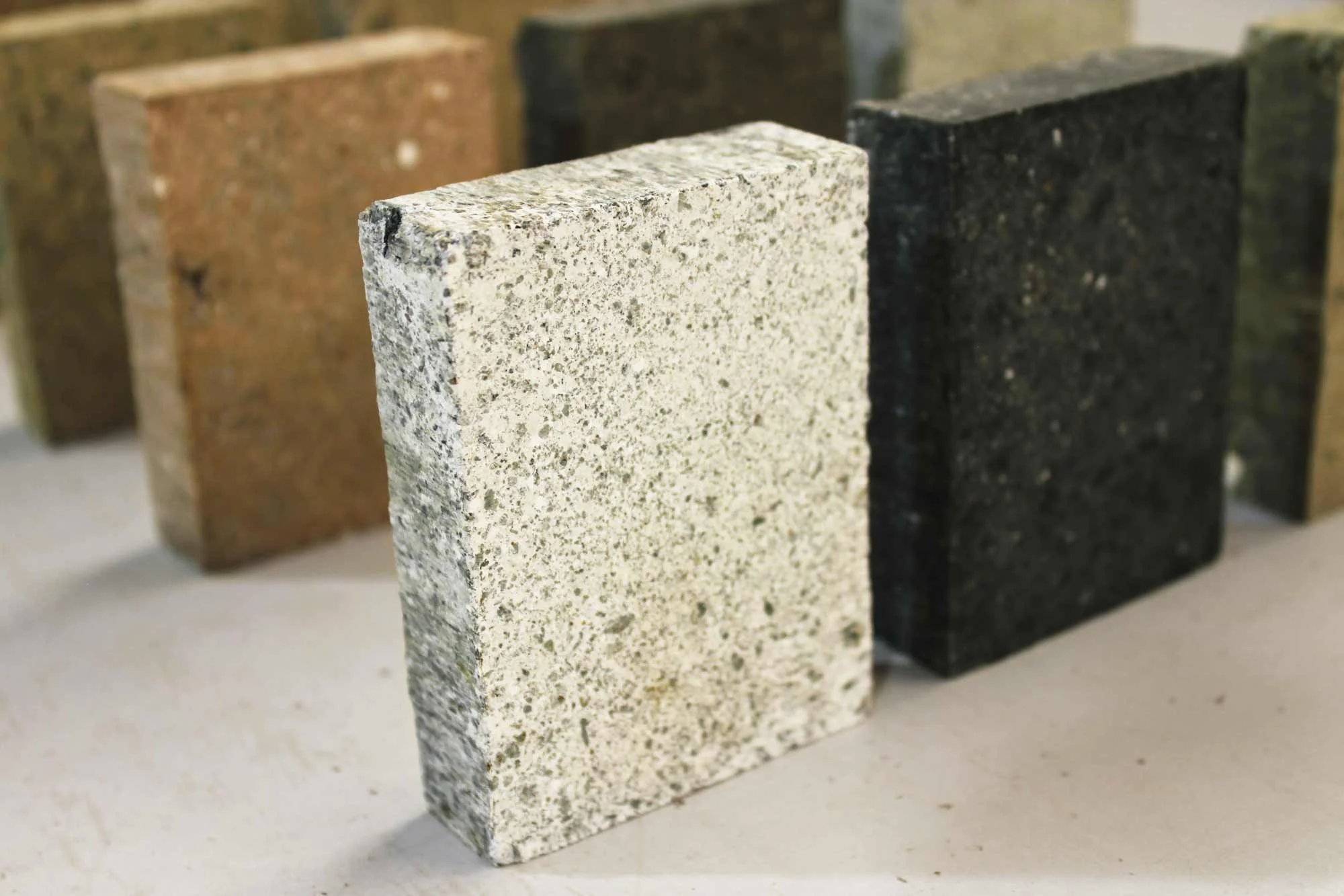 The white sample pictured here is produced from a mix design stabilized with a combination of ground-granulated blast-furnace slag, hydrated lime and lightly-colored cement. Here, the white tones are contrasted by dark basaltic aggregate. This mix design represents another example of a serendipitous aesthetic benefit resulting from employing alternatives to traditional ordinary Portland cement stabilization methodologies. Also pictured are various color samples from mix designs containing various local aggregates and mineral fines. By utilizing local aggregate and mineral materials sourced from within 50 miles of Watershed Materials' manufacturing facility, a huge range of colors and textures are attainable.