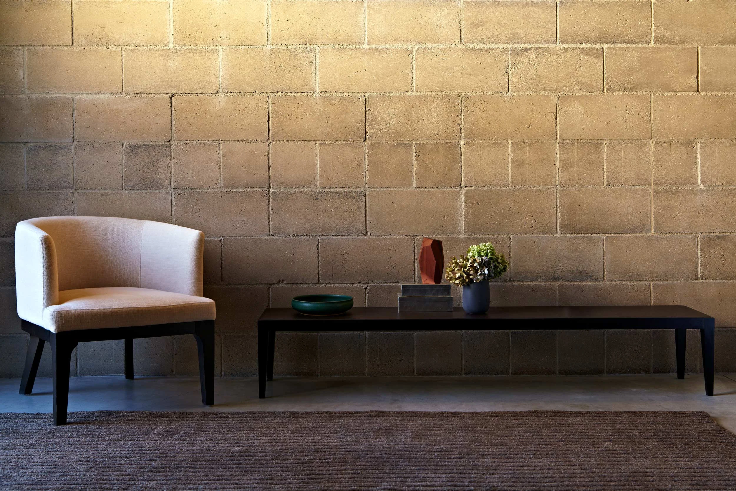 A soldier course of eight inch Pascale Watershed Blocks with a linen club chair and hand woven Odegard rug. Just as natural rock is made up of a million individual grains of quartz, feldspar, and trace elements, Watershed Blocks celebrate their unique composition. Unlike uniform concrete blocks, made of cement and dye, no two Watershed Blocks are exactly the same. Image © Jacob Snavely .