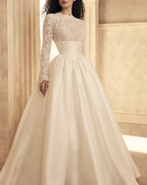 New Arrival!
Excited to share details of a new gown. It features a sheer lace bodice, a scalloped jewel neckline, and long lace sleeves, finished with fabric-covered buttons at the scalloped cuffs. These buttons continue down the center back to an em