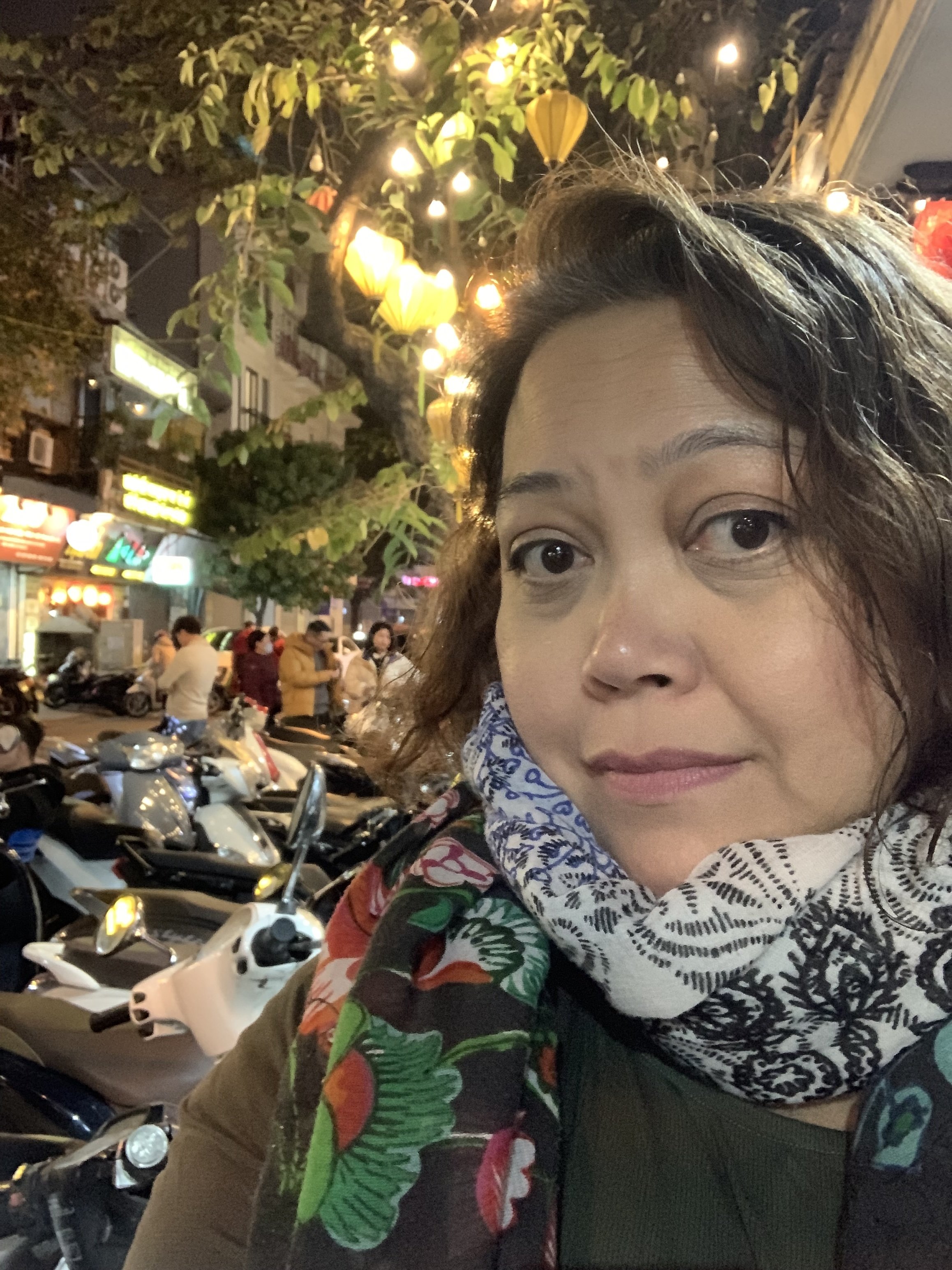 Tish Vallés on a Hanoi street at night, under glowing paper lanterns, with parked scooters behind her