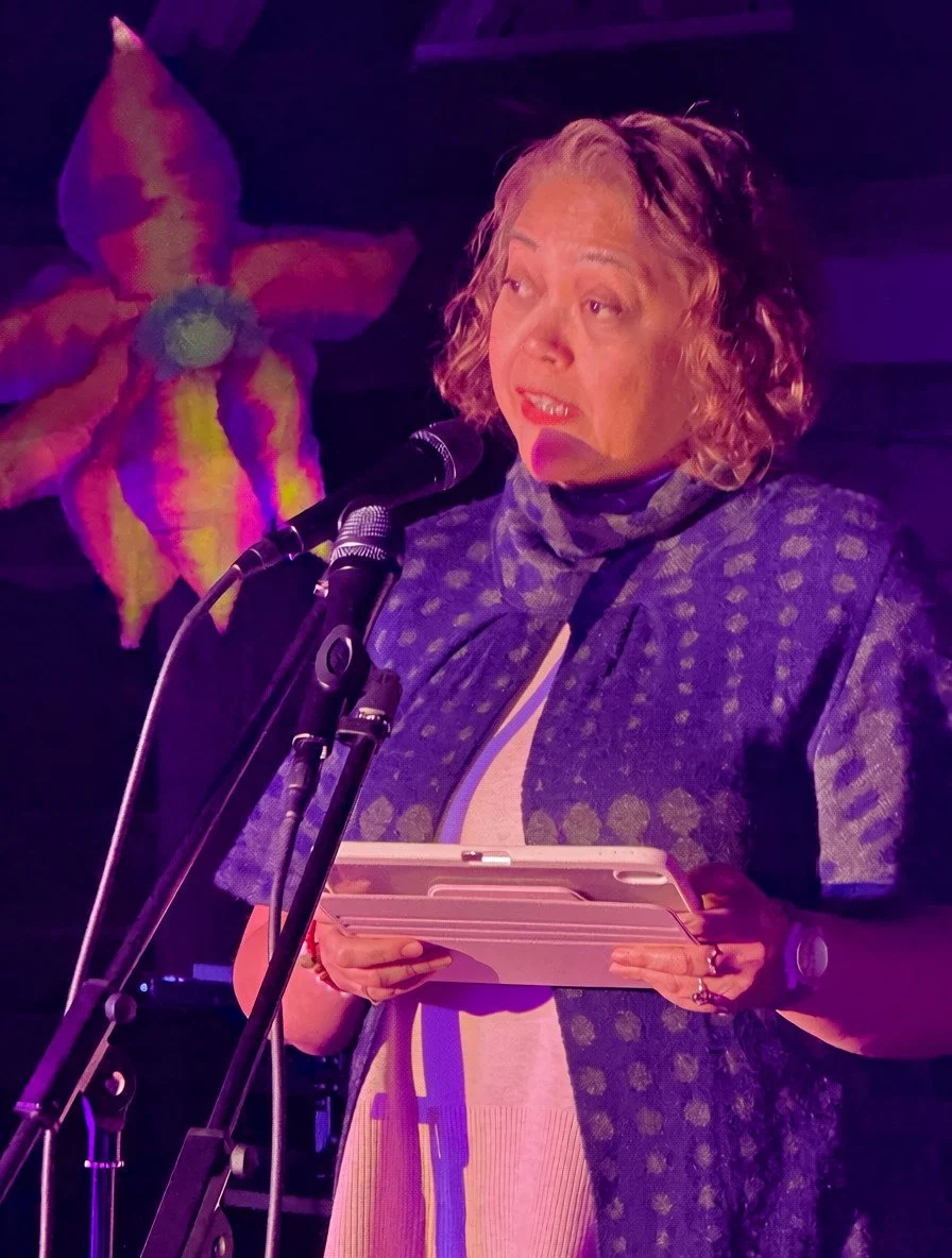 Tish Vallés reading poems at a microphone at the Lake Eden Reunion, October 2026