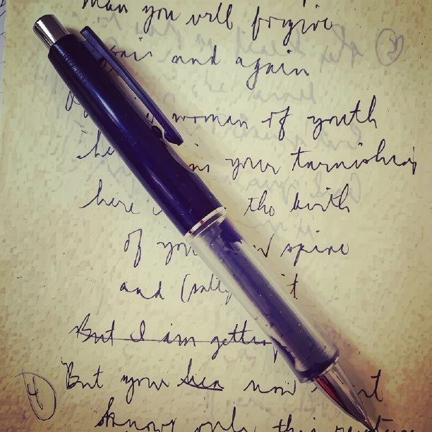 An early handwritten draft of a poem by Tish Vallés, with a pen resting across the page