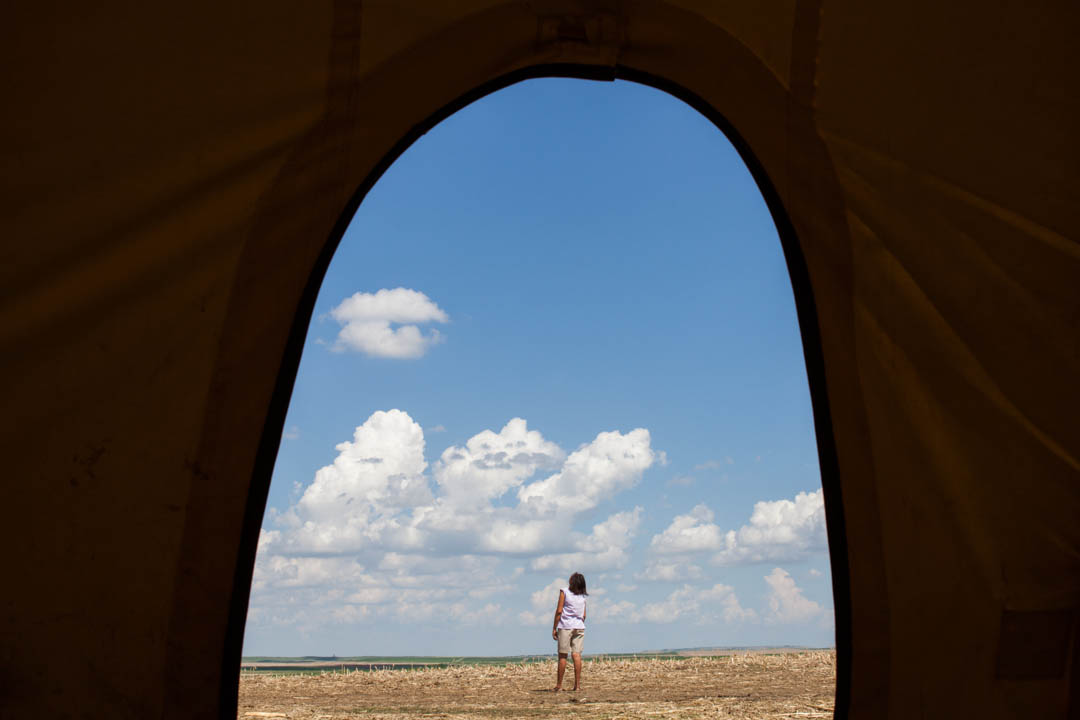 Framed by the door of a tipi, Leota Eastman-Iron Cloud watches her kite float in the air at the Oyate Wahancanka Woecun camp outside of Ideal, South Dakota. Translated into english, the camp's name means "Shielding the People" in the Lakota language. The place was installed to protest the Keystone XL pipeline and for prayer. The pipeline is proposed to cross the Rosebud Reservation at this location. May 2014