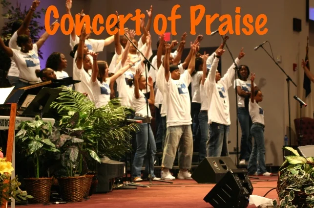 A choir of children performing on stage during a concert of praise. They are wearing white shirts and have their arms raised. The stage is decorated with green plants, and there are microphones and speakers visible. The words "Concert of Praise" are displayed in orange text at the top of the image.