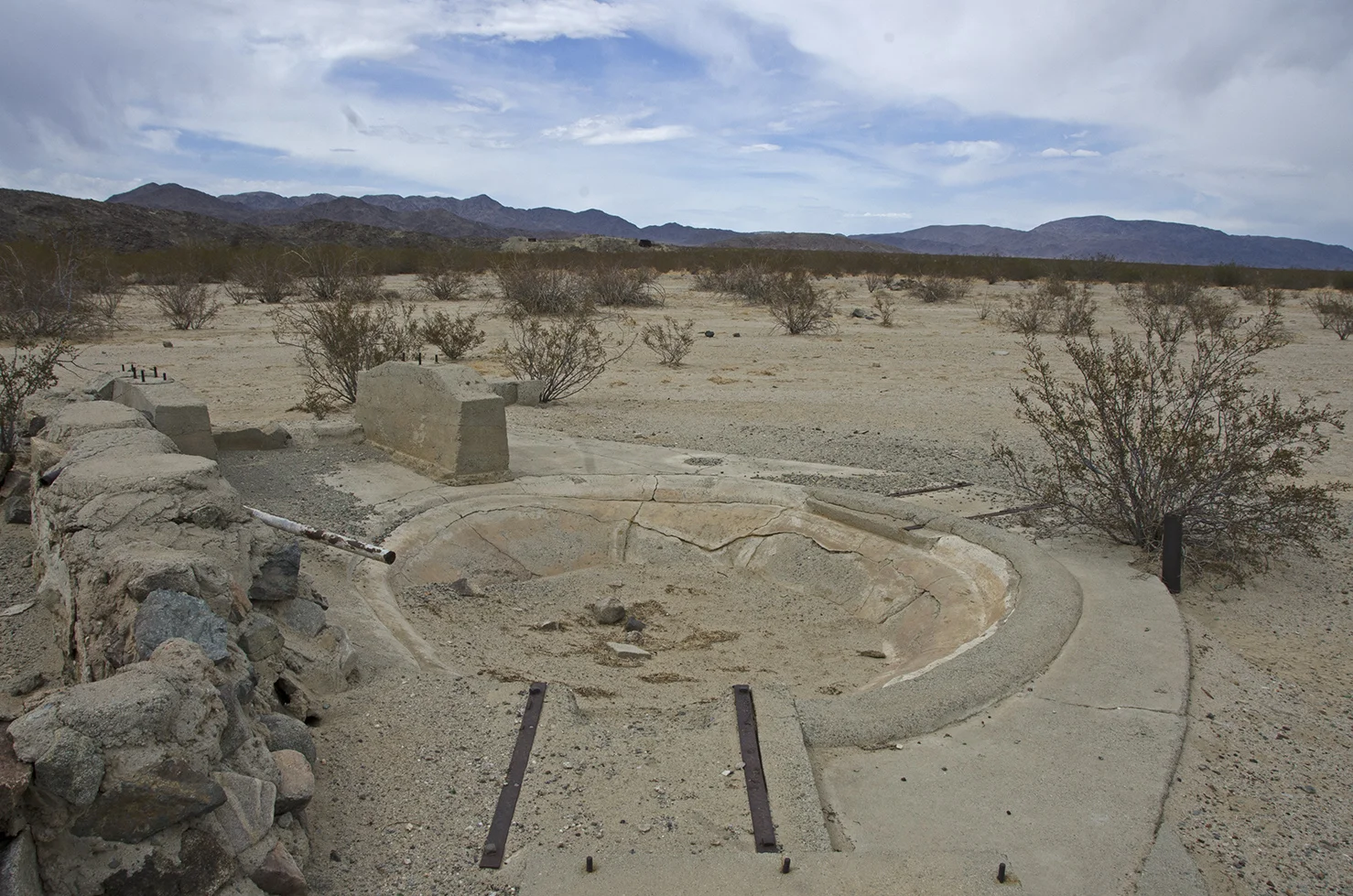 A small, concrete settling basin located next to the stone-walled vat.