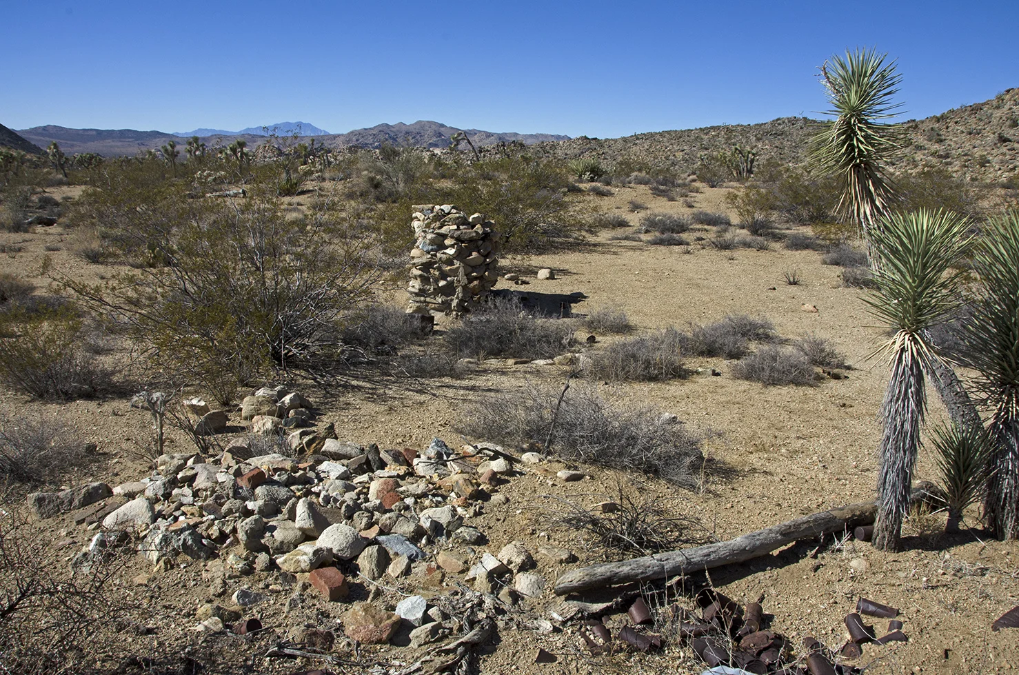 Pile of rubble stones, outline of rock flower garden, and stone fireplace, front to back