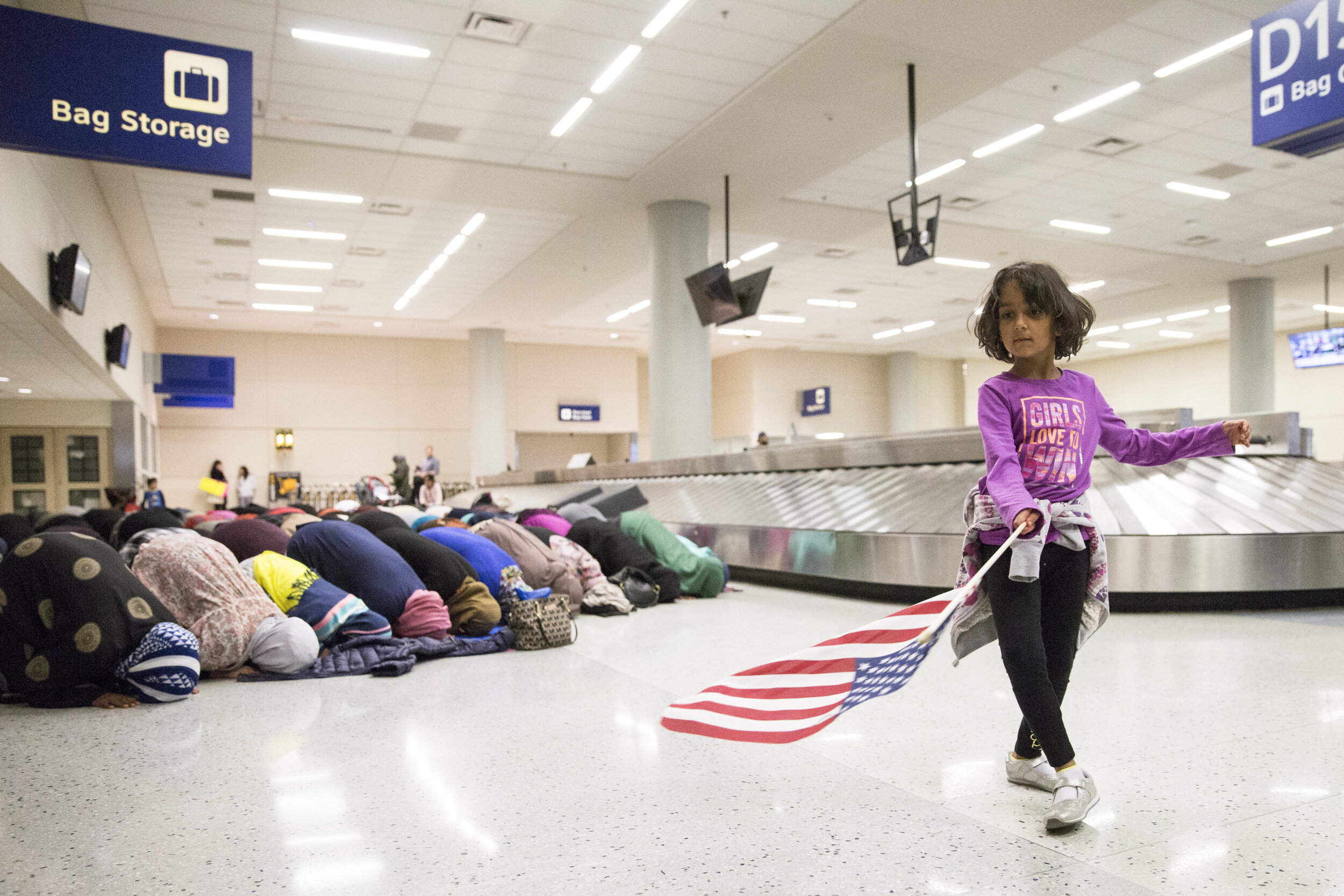  A young girl dances with an American flag while protestors take a moment for prayer during protests against Donald Trump’s travel ban at DFW Airport. 