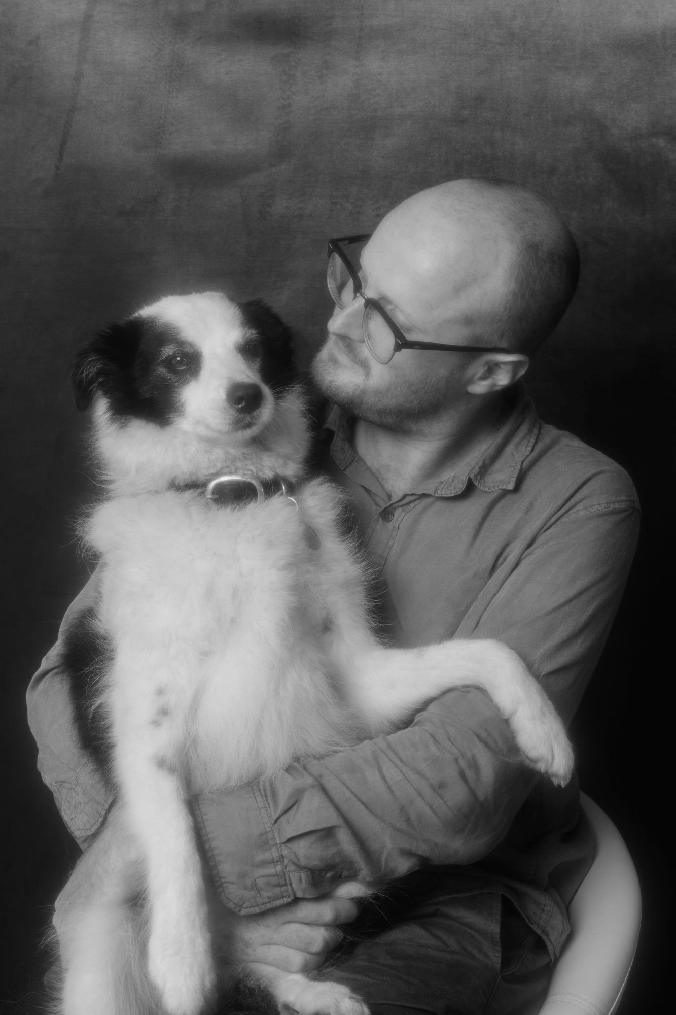 A black and white photo of a man holding a dog and looking at it affectionately.
