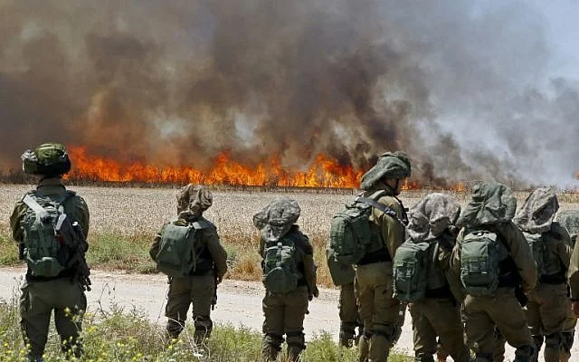 Israeli soldiers walk amidst smoke from a fire in a wheat field near the Kibbutz of Hahol Oz, along the border with the Gaza Strip, which was caused by incendiaries tied to kites flown by Palestinian protesters from across the border (May 14, 2018 - Jack Guez/AFP)