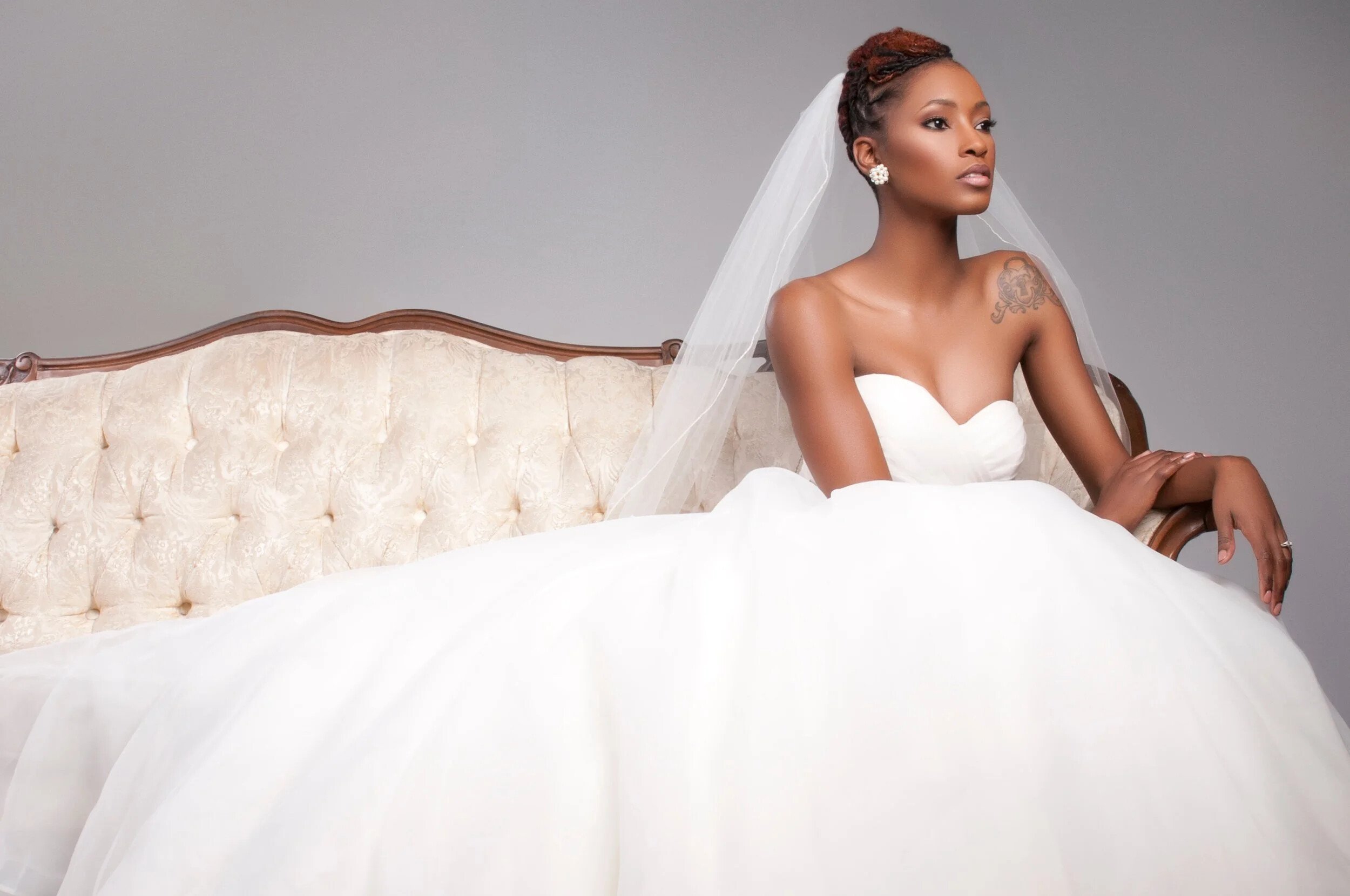 Bride seated on a cream chaise with soft glam bridal makeup by Keena Queen