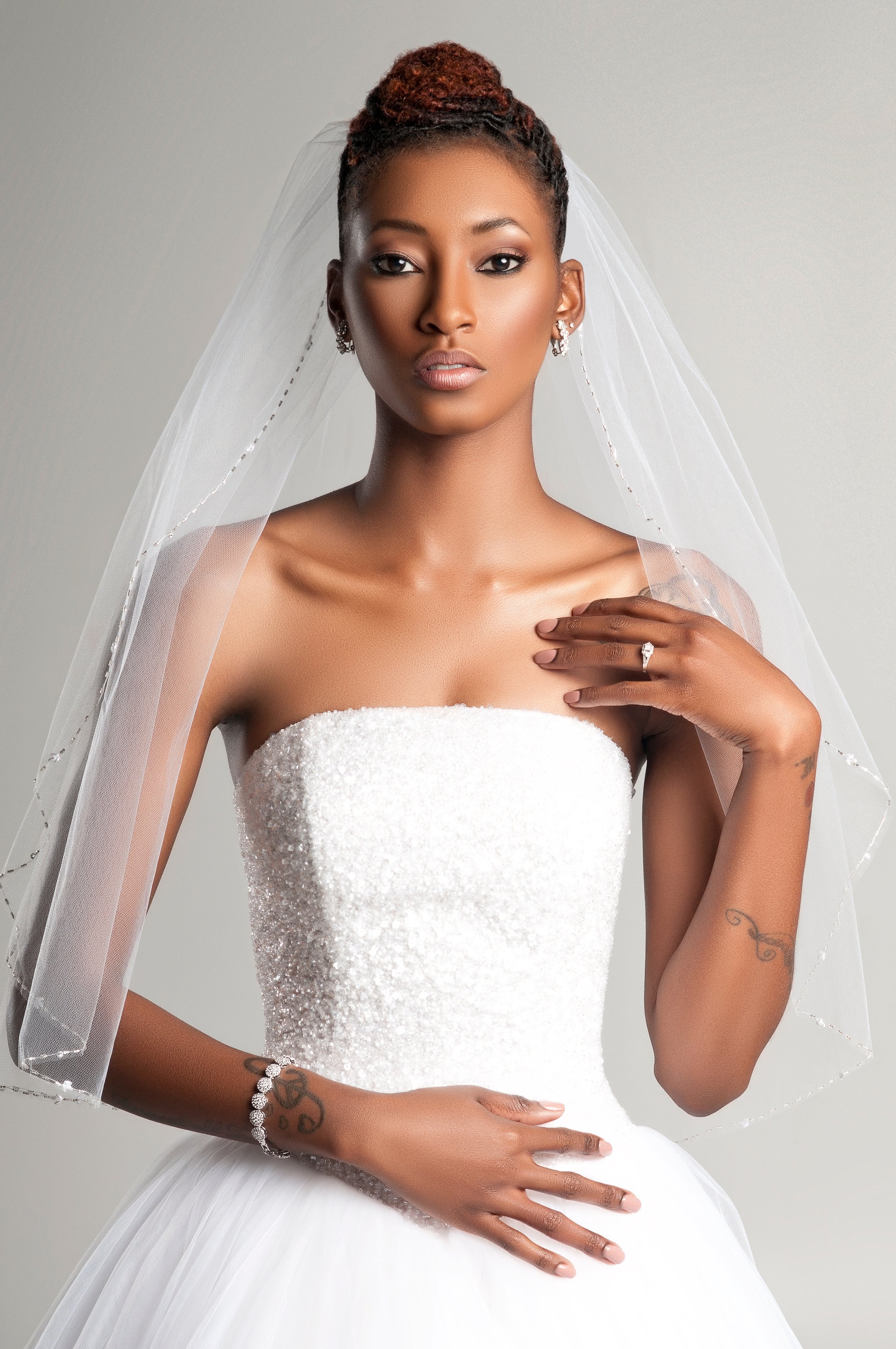 Bride in a strapless lace gown and veil, one hand at her shoulder, neutral bridal makeup
