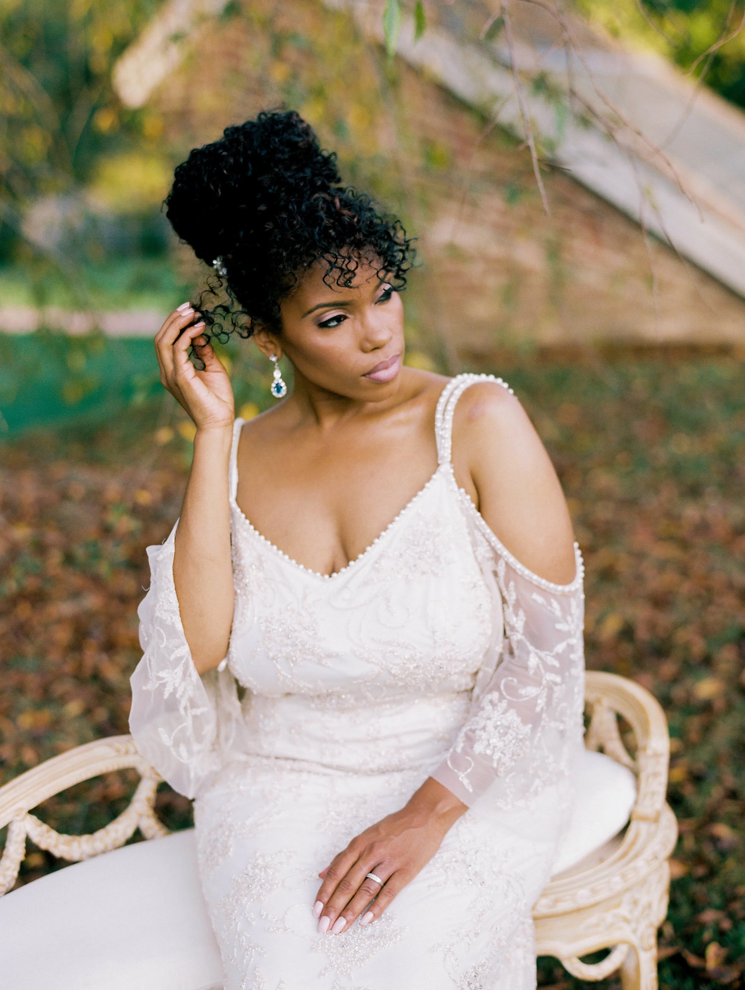 Bride with curly updo in an off-shoulder lace gown seated outdoors