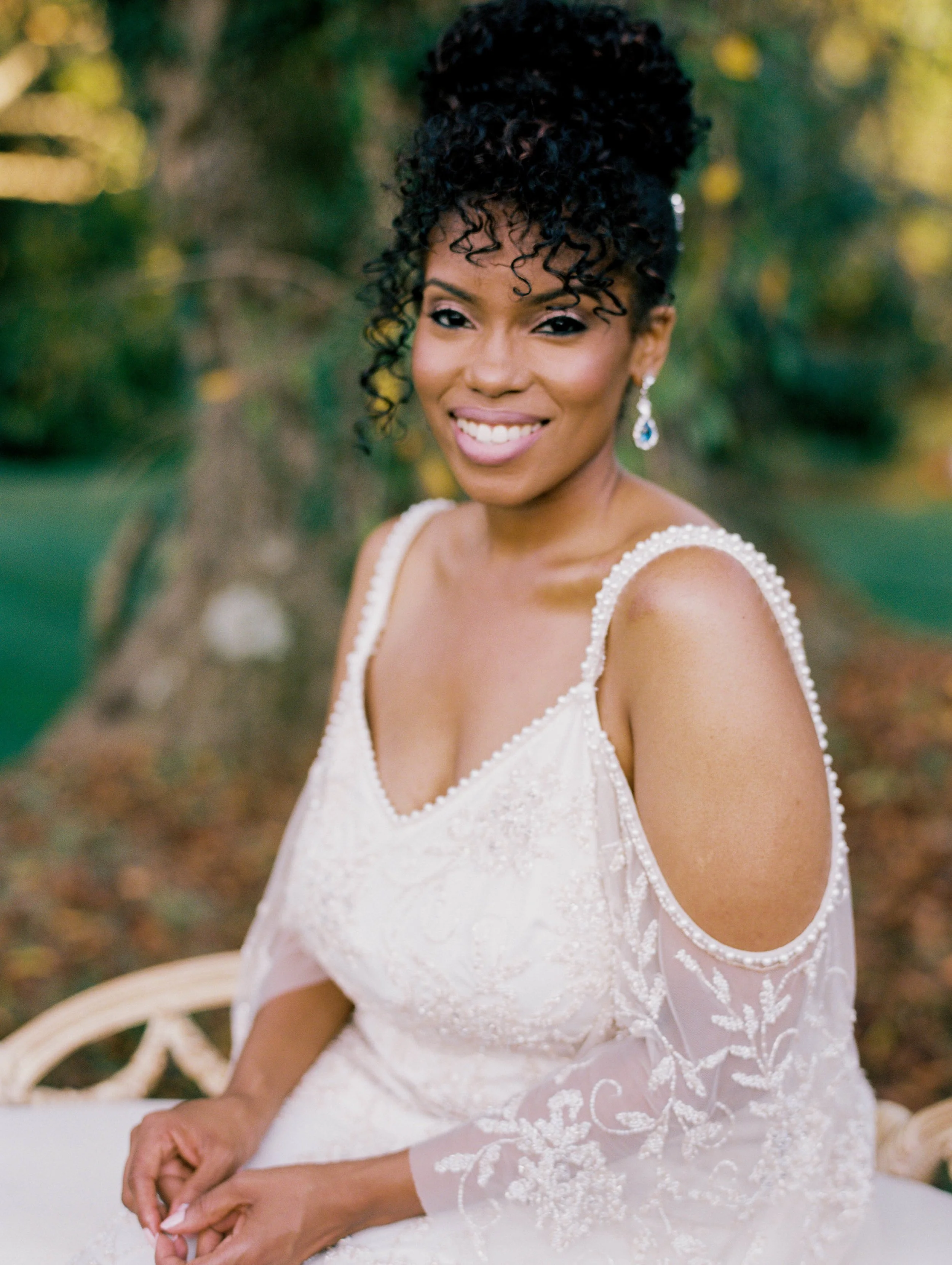 Bride in a cold-shoulder lace gown seated outdoors, smiling