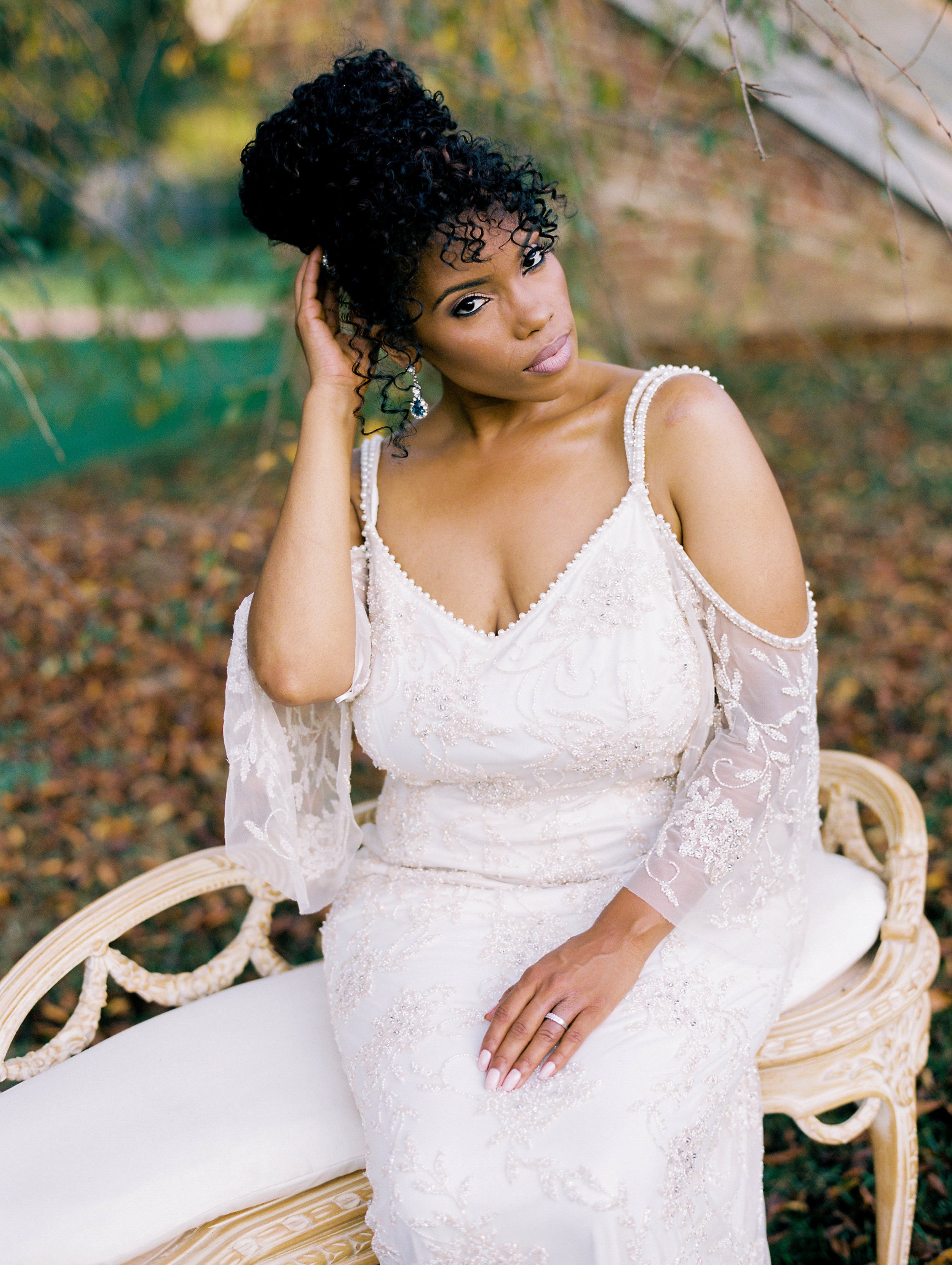 Bride with braided updo in a cold-shoulder lace gown seated in a garden chair