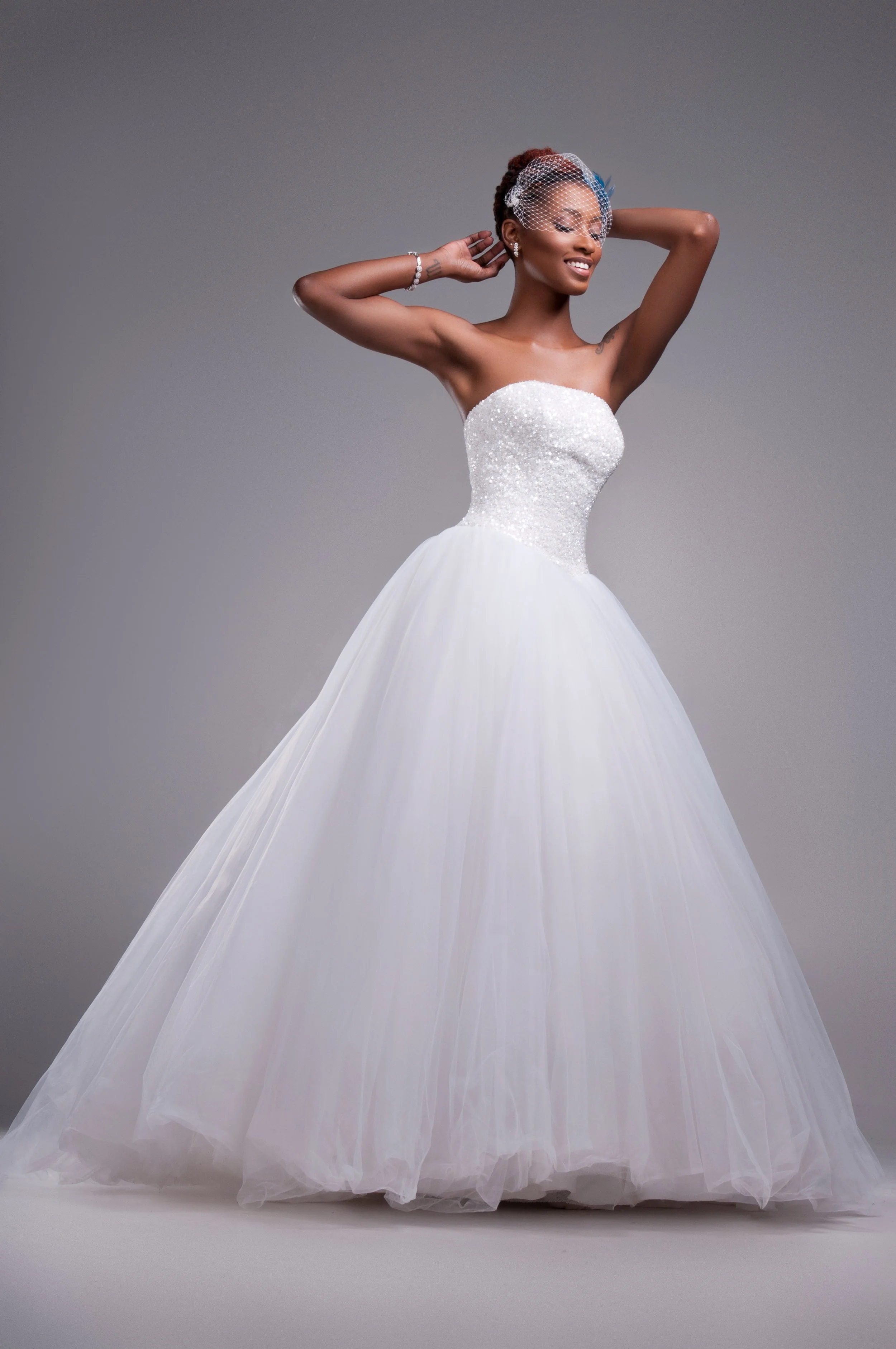 Full-length bride in a ballgown with an updo, hands raised to her hair, studio portrait
