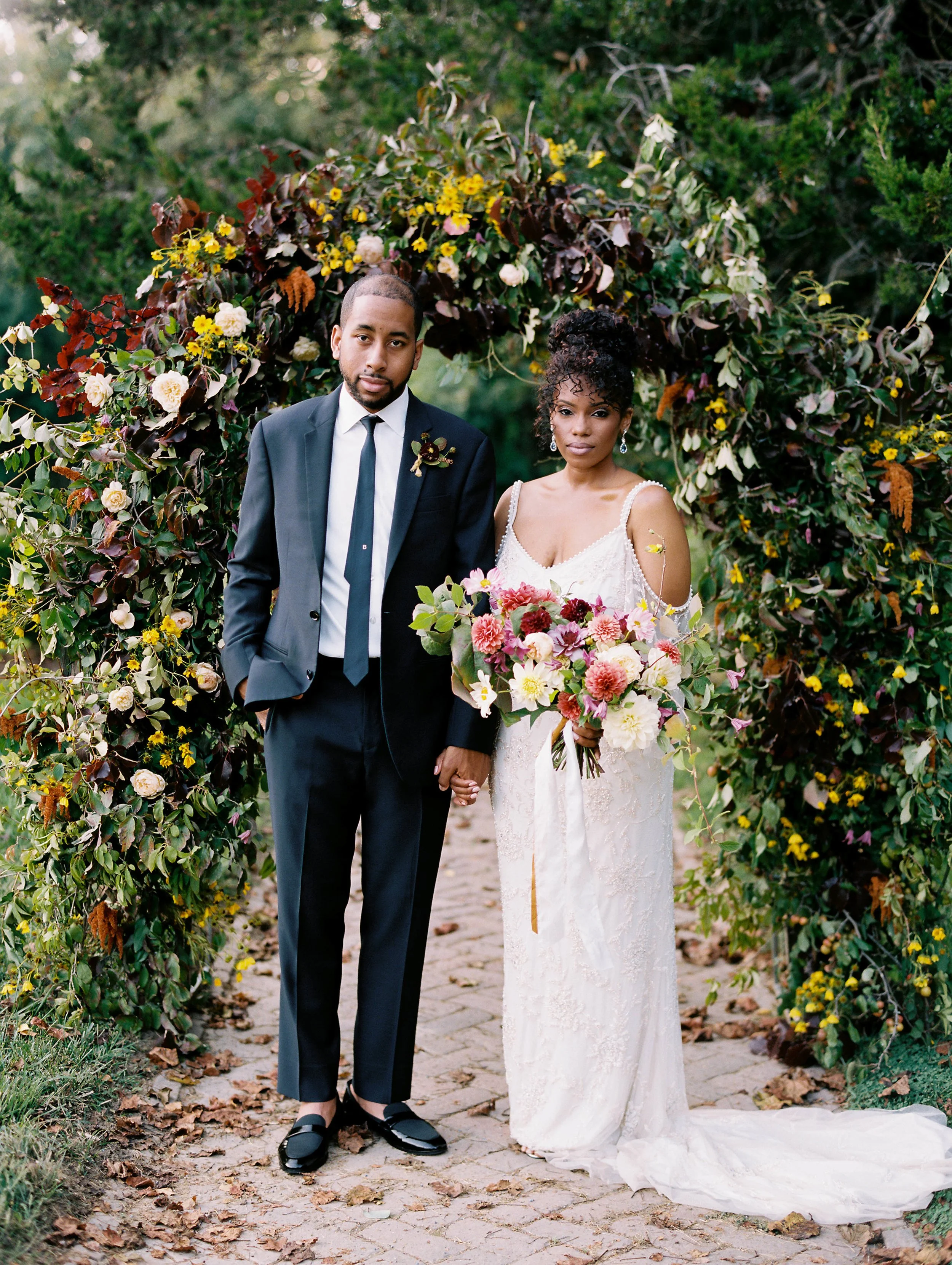 Bride and groom on a tree-lined garden path, bride holding a bouquet