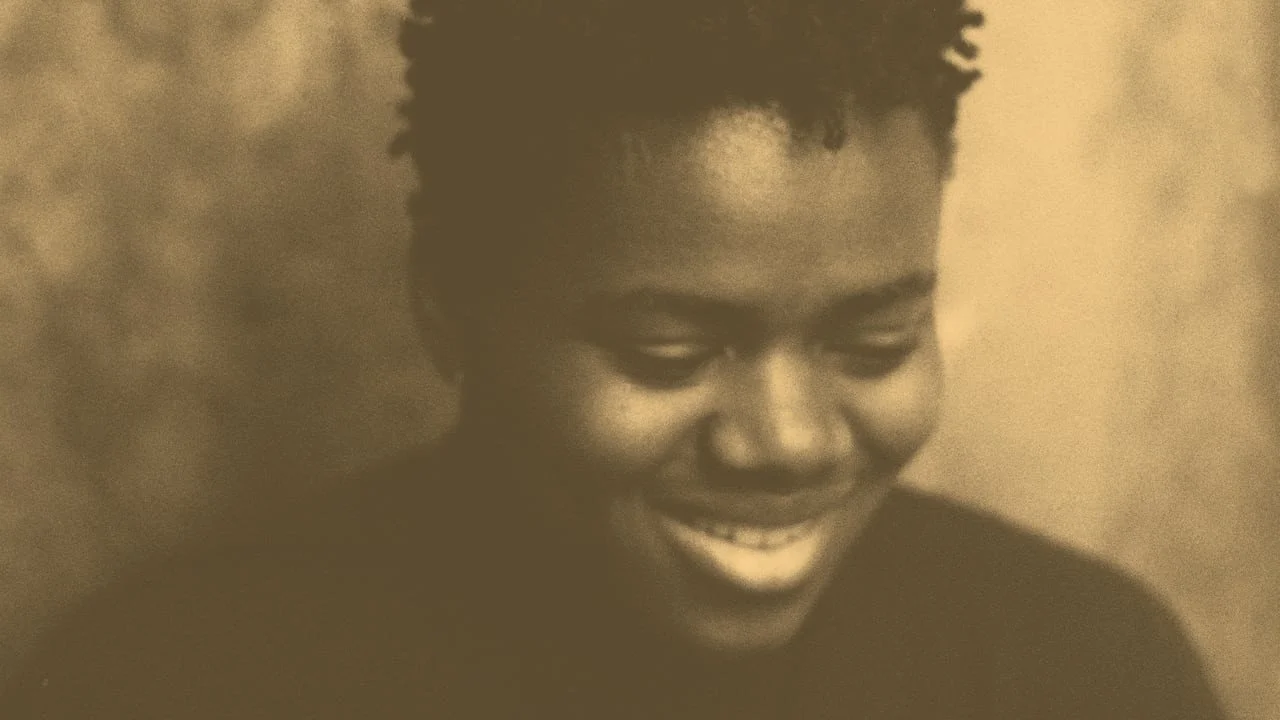 The picture depicts a close up of Tracy Chapman smiling well looking down. The photo has a sepia filter on it.