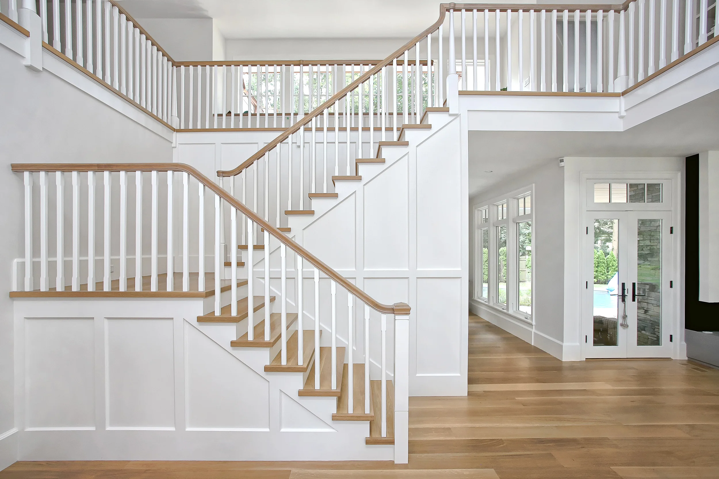 This is the view once you enter the front door. The Living Room is to the right, the Dining Room is behind the stair, and an open space leading to the Kitchen, Office, Mudroom and secondary stair is to the left. This central stair is a central figure between all of these spaces. We panelized the stair and left all other wall treatments as smooth painted surfaces to emphasize the figural quality of the stair as a piece of millwork. Chunky stair treads and handrails are finished to match the floor in this light filled space.
