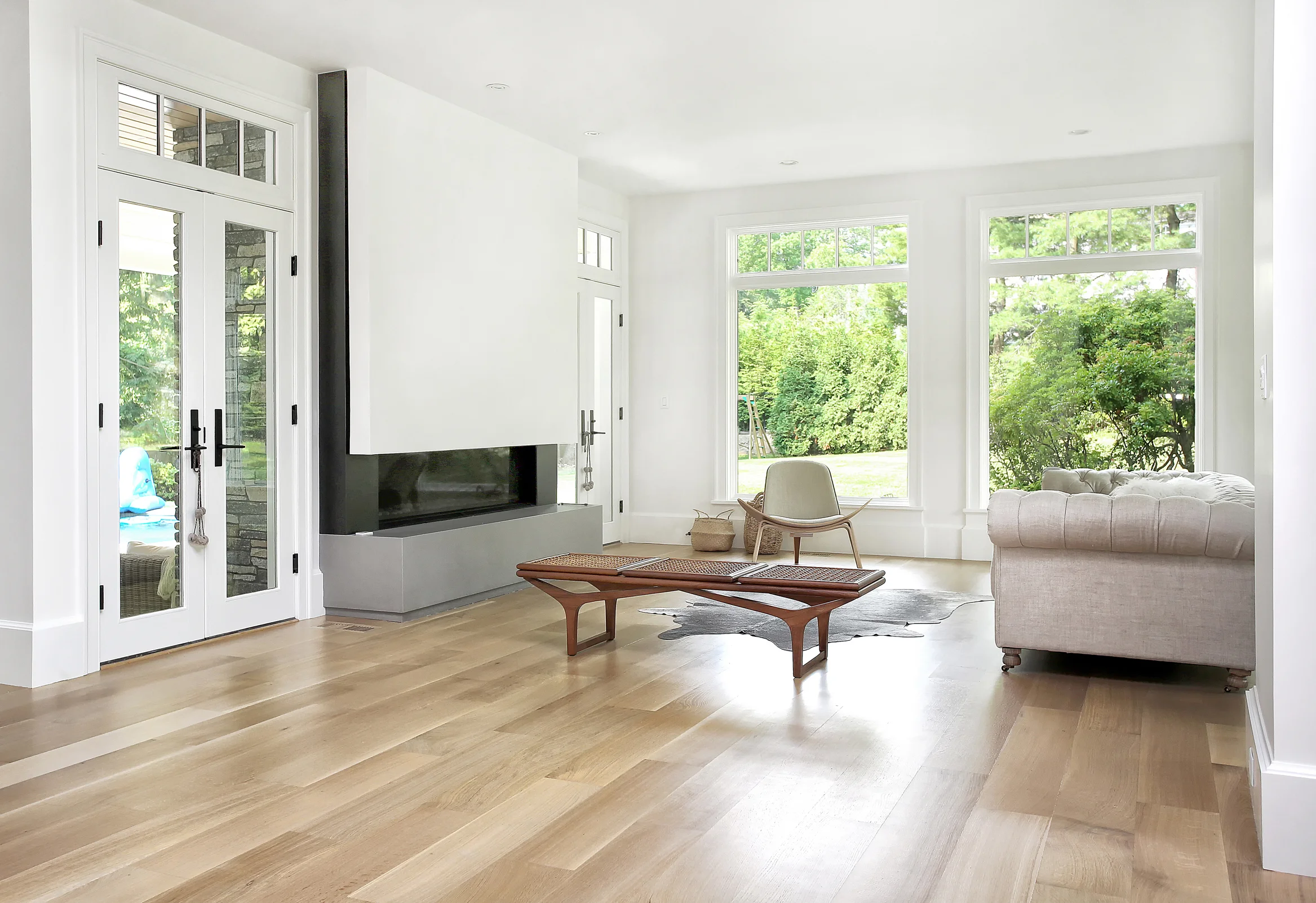 This is the view from the entry into the Living Space. We designed a 6 foot long by 12 inch high gas fireplace which provides a linear flame. We surrounded this firebox with blackened steel panels, and designed a custom gray quartz hearth. This entire space is wrapped in large picture windows with transoms above to provide maximum light to the interior and transparency to the rear yard and pool area.