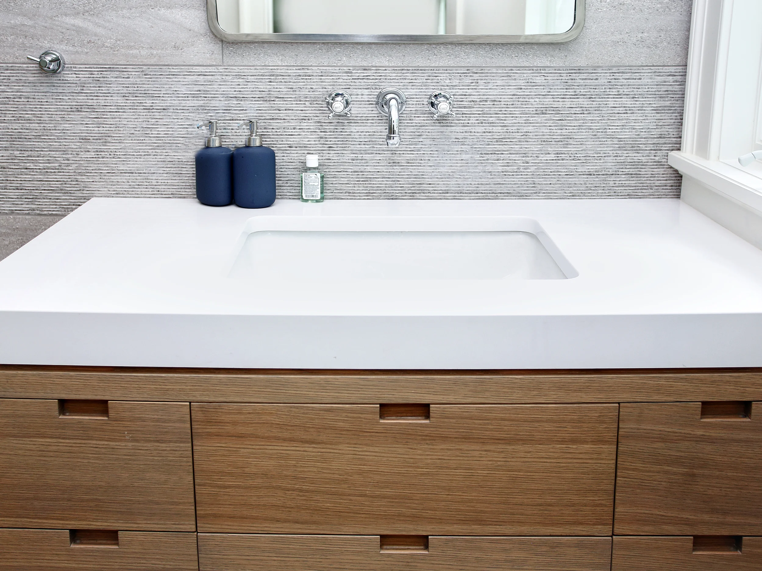 In the boys bathroom, large shower and wall behind the vanity were clad in a porcelain tile that resembles concrete. We used alternating bands of two textures along the full height of the walls. The vanity is a custom white oak cabinet with built-in finger pulls. The counter is a mitered white quartz counter so that the edges appear 3" thick. The countertop material and cabinet are seperated by a 3/8" reveal to give a shaddow and finished look to the flush condition.