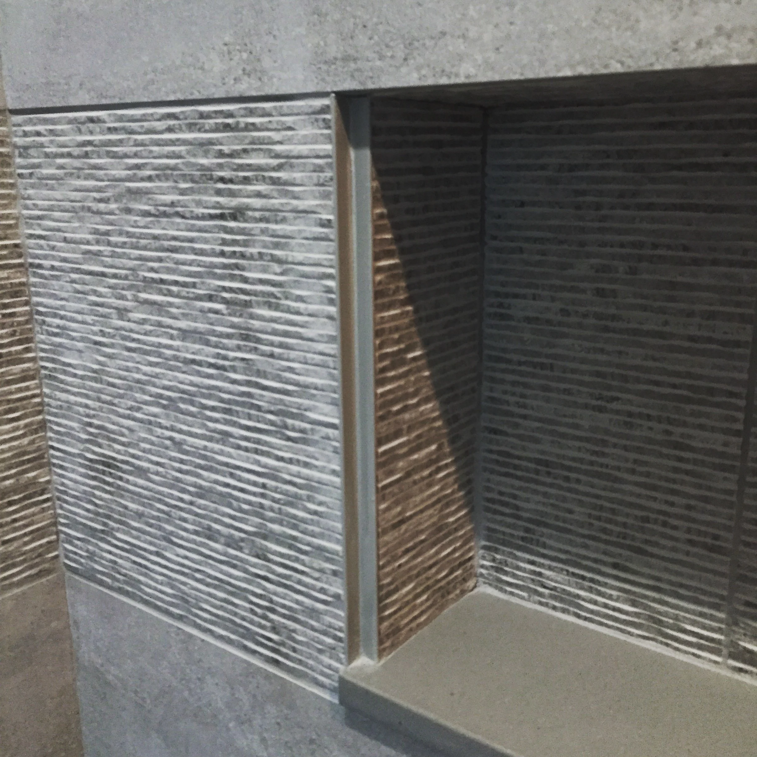 We designed a 5 foot long soap/shampoo recess in the shower that exactly conforms to the height of the textures wall tile. Because the cut edges of porcelain tile is unfinished, we used a brushed stainless steel corner trim to finish the recess which exactly meets the side edge of the gray quartz slab below. All of these alignments when done well look easy. But it takes a lot of care and attention all the way back into the rough framing stage of construction to get it right.