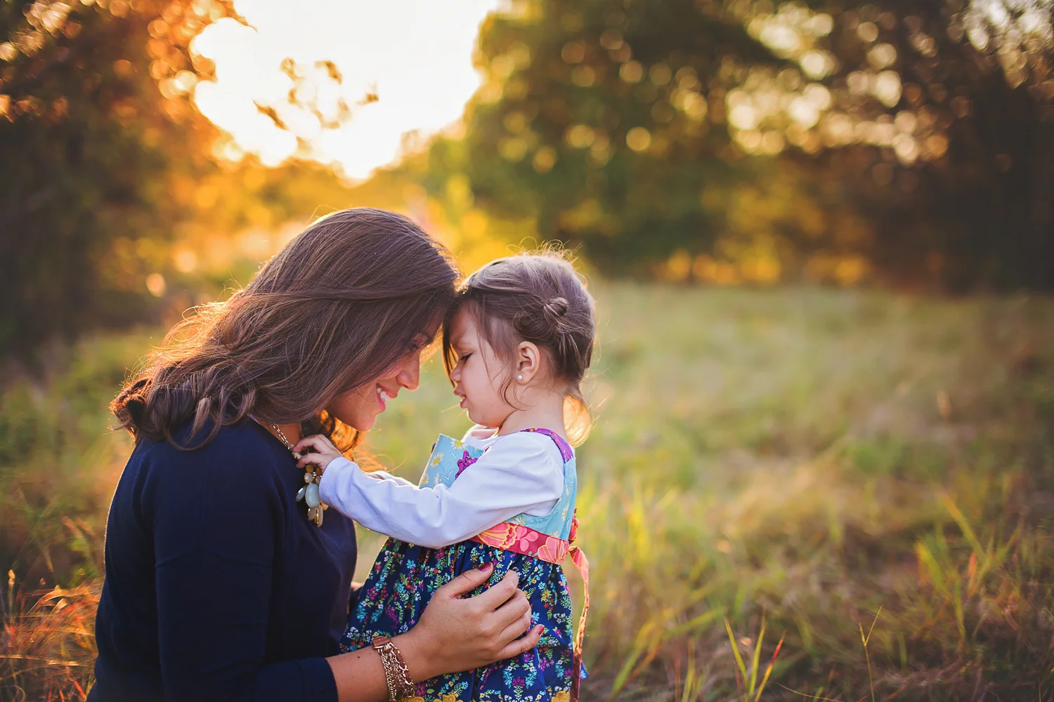 Mother and daughter lean into each other for intimate motherhood portrait in a field.