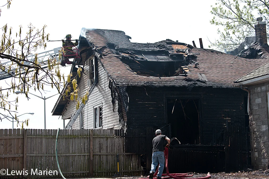 Carbondale Fire Department firefighter Bradley Lam checks for hotspots on the roof of 208 W. Hospital Drive in Carbondale while another firefighter rolls up a fire hose next to the back wall of the house.
