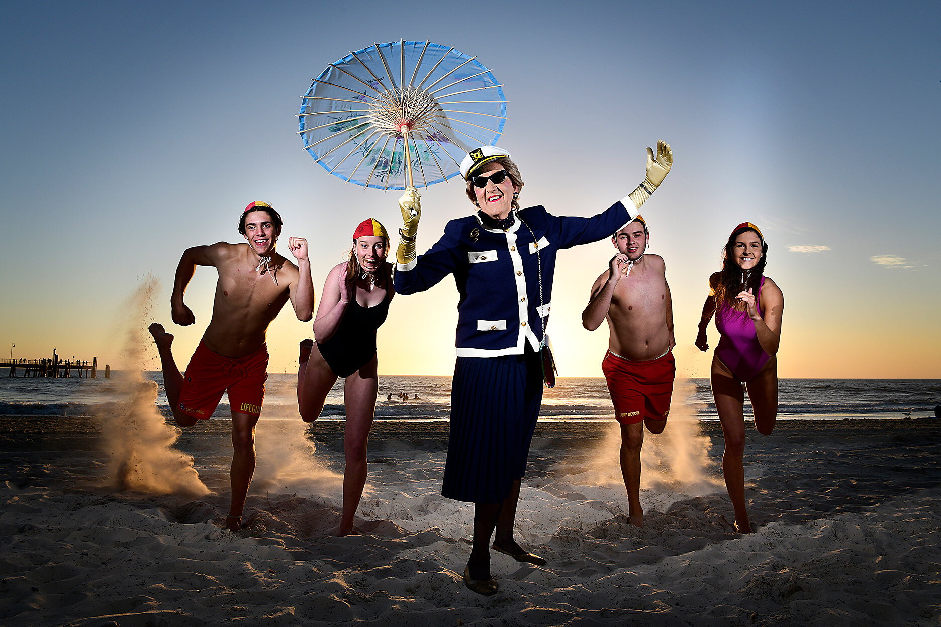  14.9.18 -  Dr. Gertrude Glossip with surf lifesavers Cooper Forest, TJ Walkden, Edward Gates &amp; Brittany Jessup at Glenelg Beach. Dr. Gertrude Glossip is the alter ego of Will Sergeant - Feast Ambassador, who is showcasing his event in the Feast 