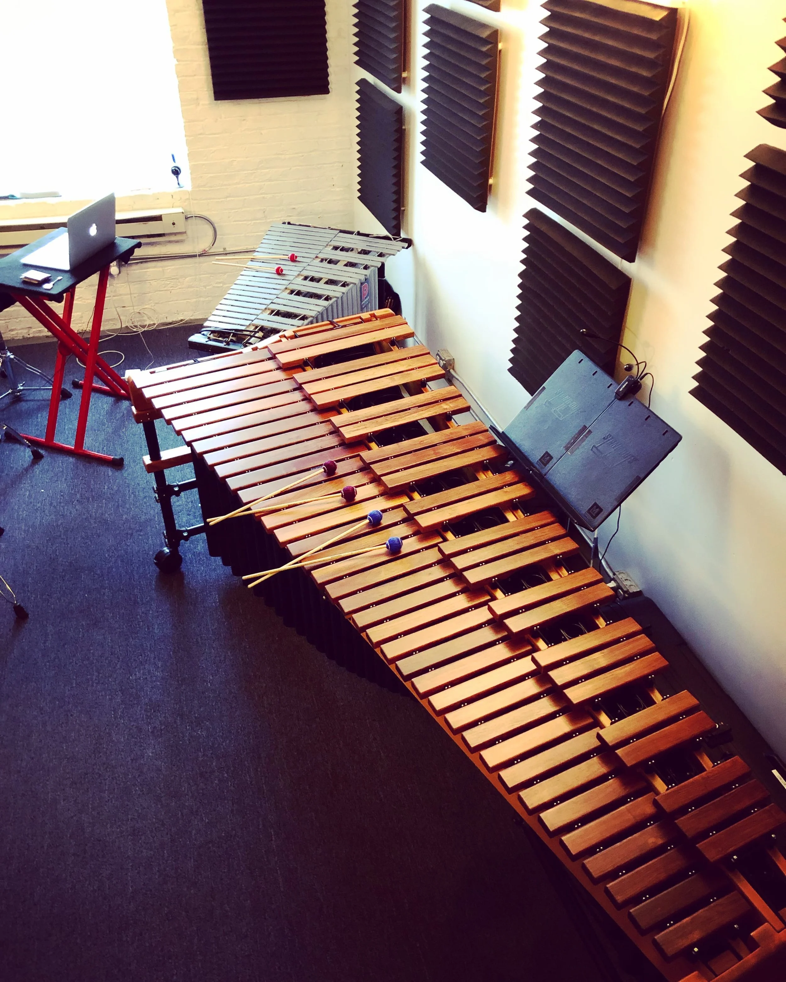 Music studio with marimba, a vibraphone, a laptop on a chair, and soundproofing foam on the walls.