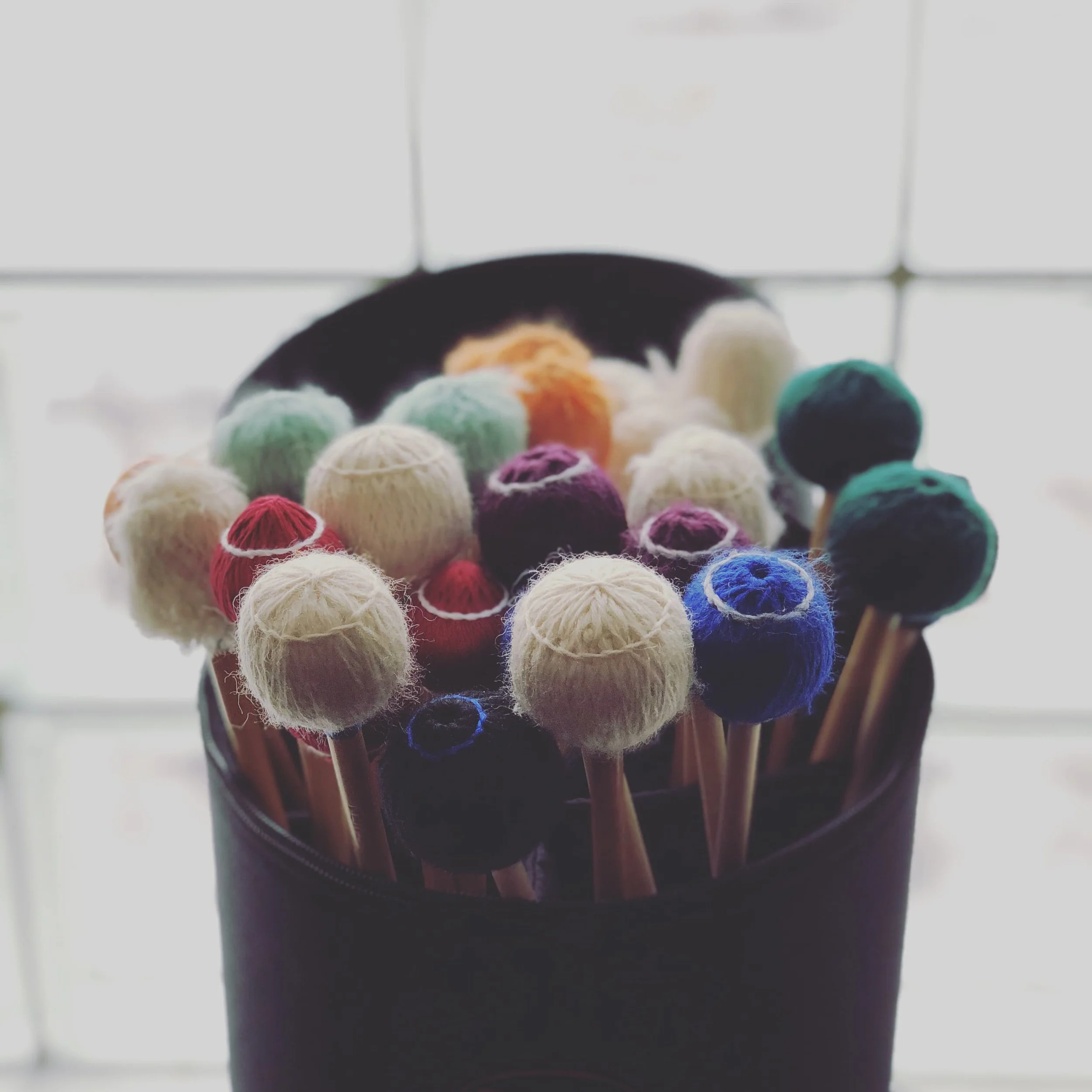 Close-up of colorful yarn mallets organized in a stick bag against a glass panel window.
