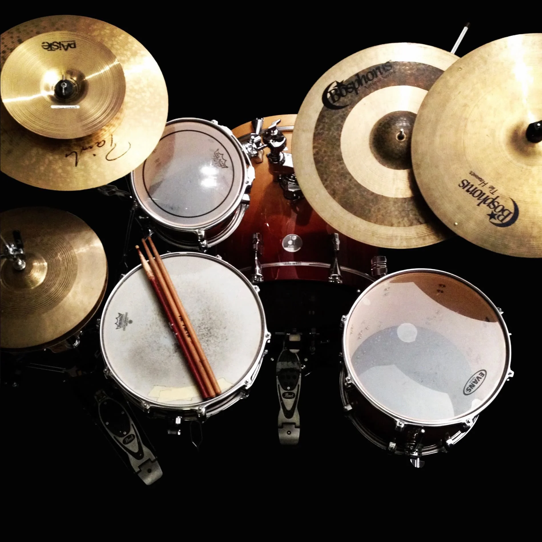Top-down view of a drum set with cymbals, snare drum, and sticks on a black background.