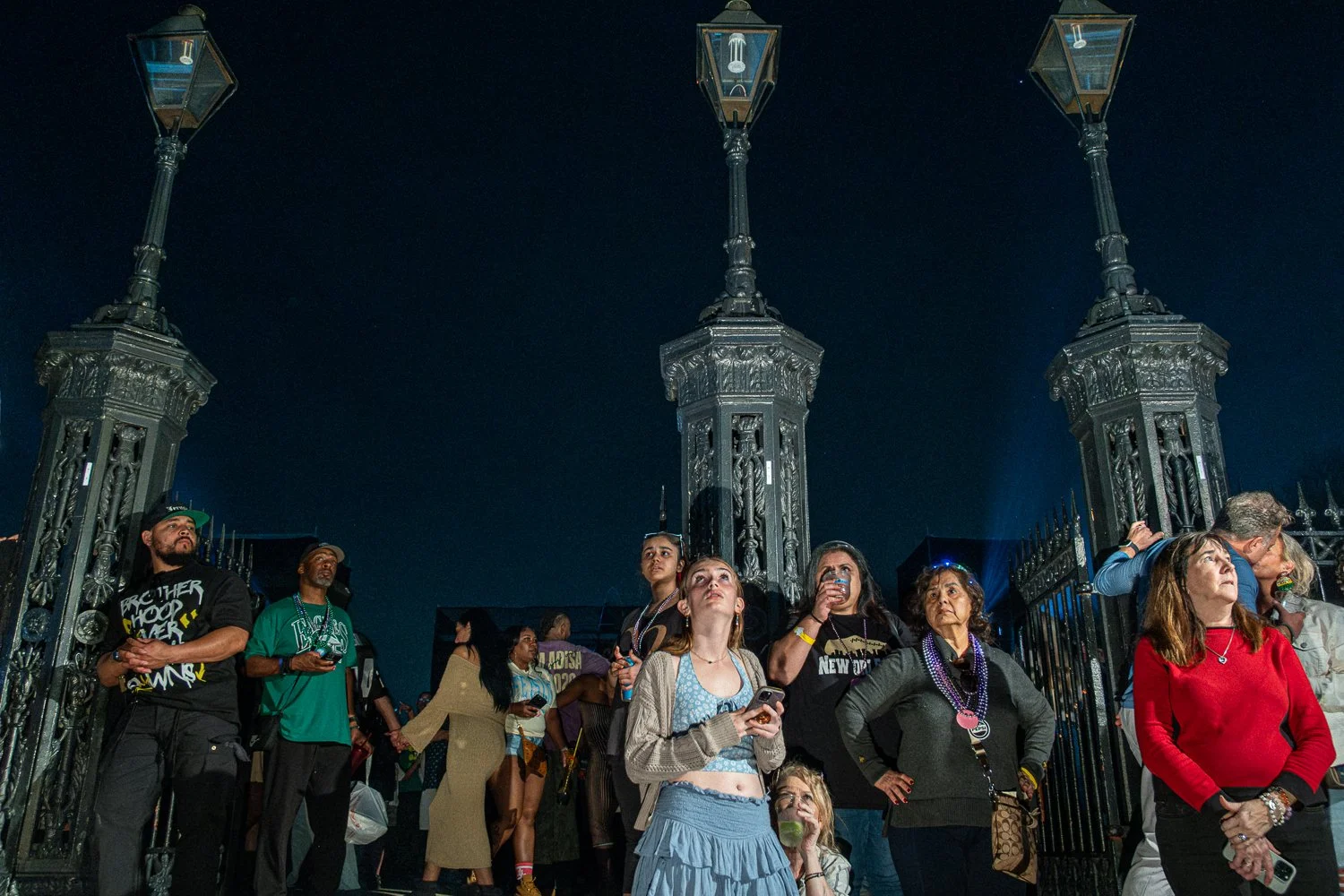 Fans gather in Jackson Square in the French Quarter at night during Super Bowl week in New Orleans, with one couple kissing.