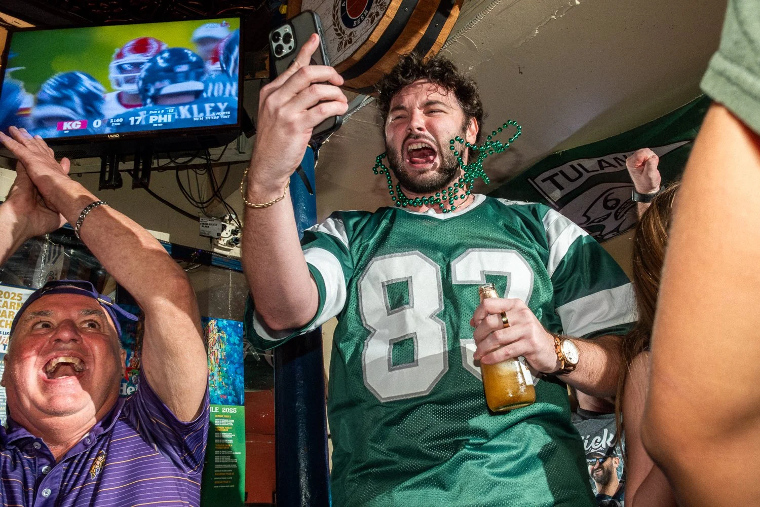 Local Eagles fans jump and cheer inside a New Orleans bar as a touchdown is shown on television, with one fan’s beads caught midair around his neck.