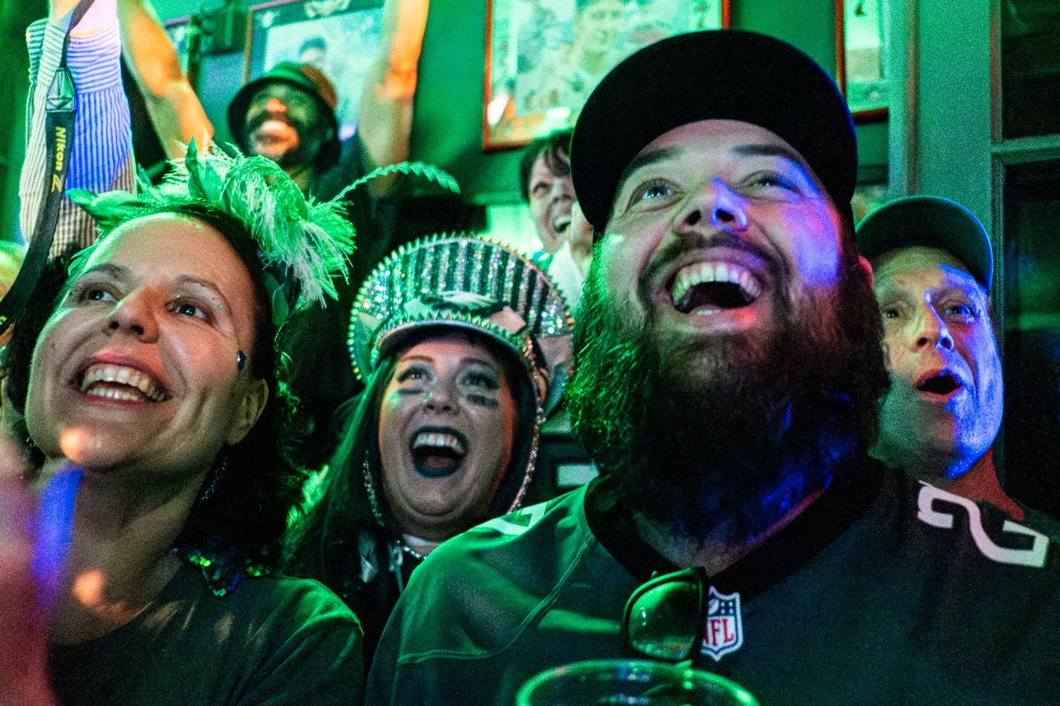 Eagles fans in costume watch the final minutes of the Super Bowl at Markey’s Bar in New Orleans, smiling as they look up at the screen.