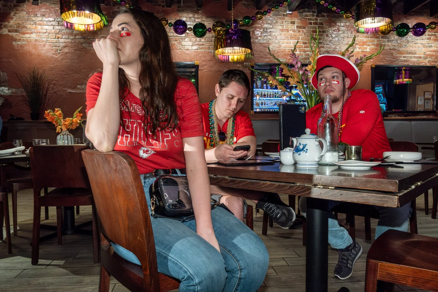 Kansas City Chiefs fans sit at a table inside a New Orleans restaurant during the Super Bowl, with one man looking at his phone.