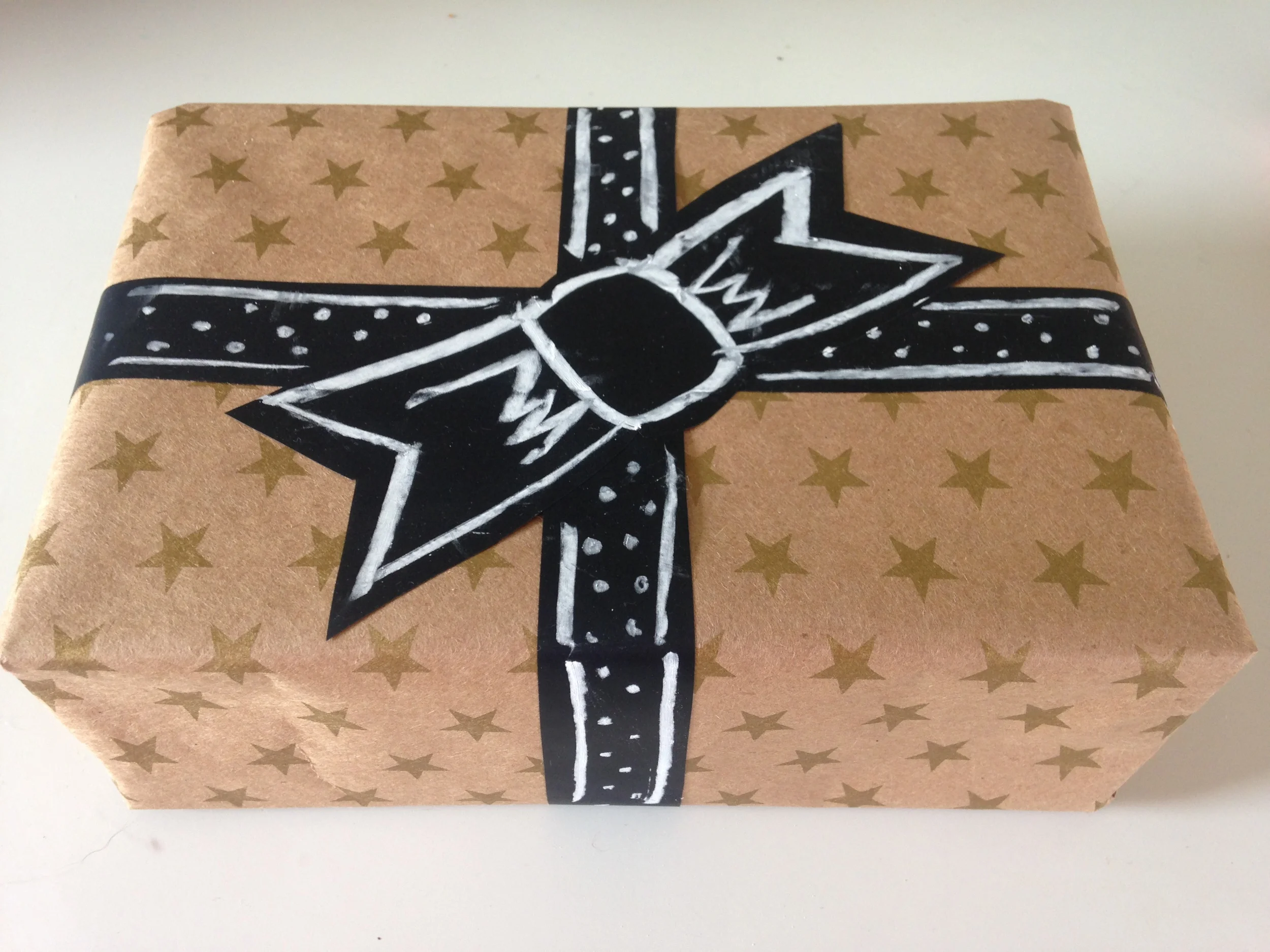 I'm always scrambling around my house to find gift wrapping materials in decent shape, and rarely do I have cute ribbon on hand. Chalkboard tape saves the day! I wrapped this gift with leftover christmas paper and cut out a ribbon and bow to apply to the box. Then I scribbled a quick design to make it look intentional . 