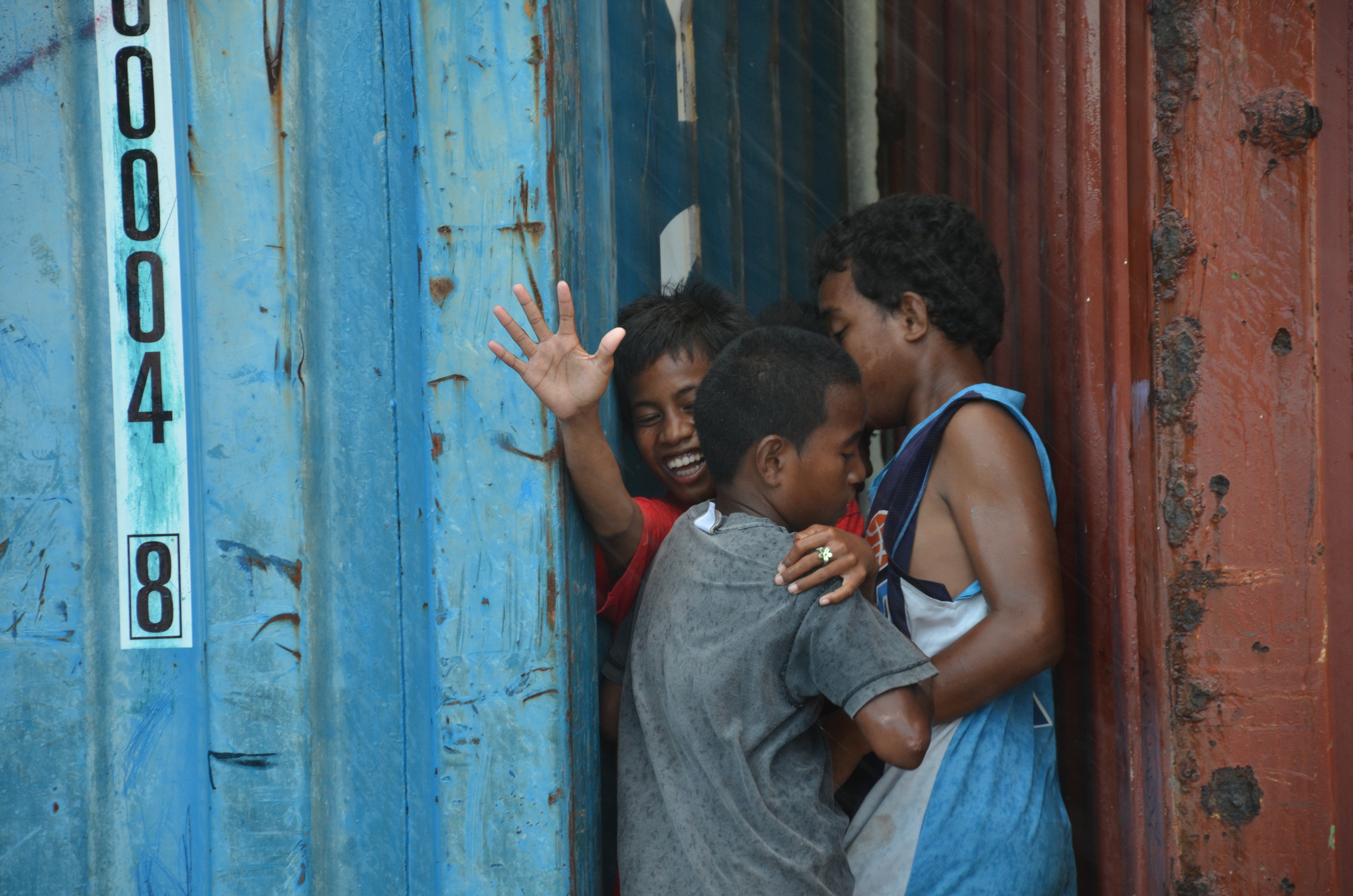  During a sudden rainstorm, children seek shelter between shipping containers. 