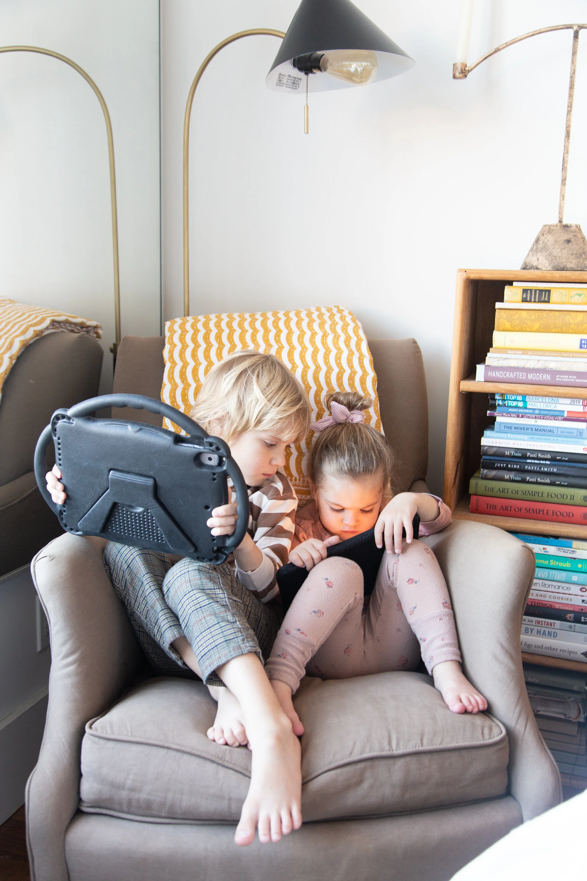  two children on ipads in a chair in the corner. 