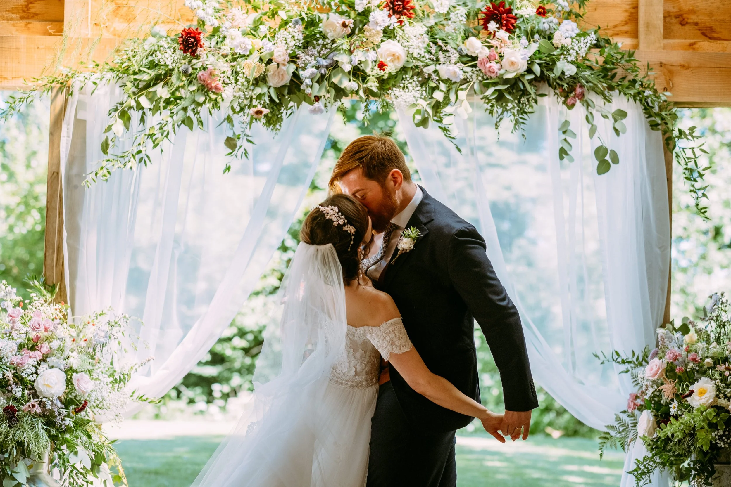 Bride and groom having their first kiss in front of flowers