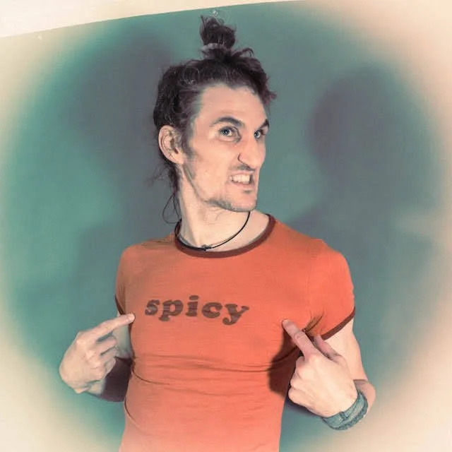 Person with a playful expression pointing to a shirt that says 'spicy' in bold letters.