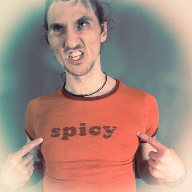 A person with an intense expression pointing at a red T-shirt with the word 'spicy' printed on it.